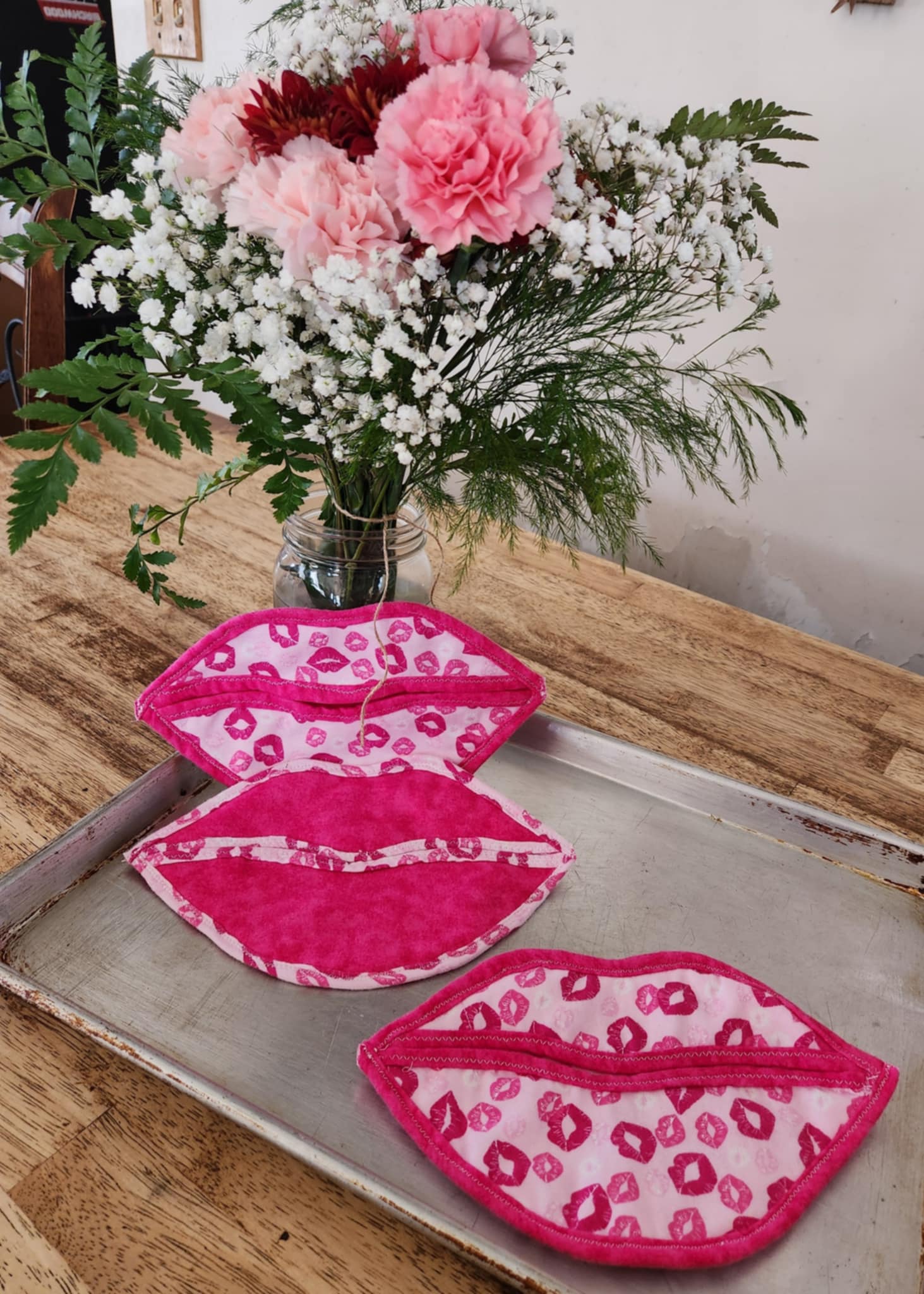 Hot pad shaped like a lips with light pink background with pink kisses seal flap and the rest a bright pink