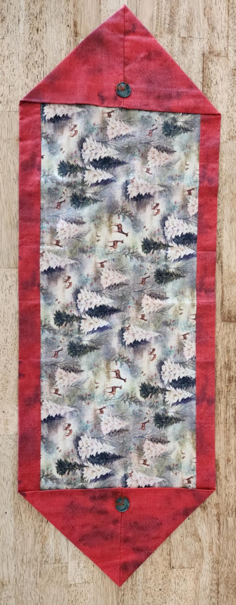 A table runner with triangle ends and the border is red. The inside is trees and deer with sparkle patterns