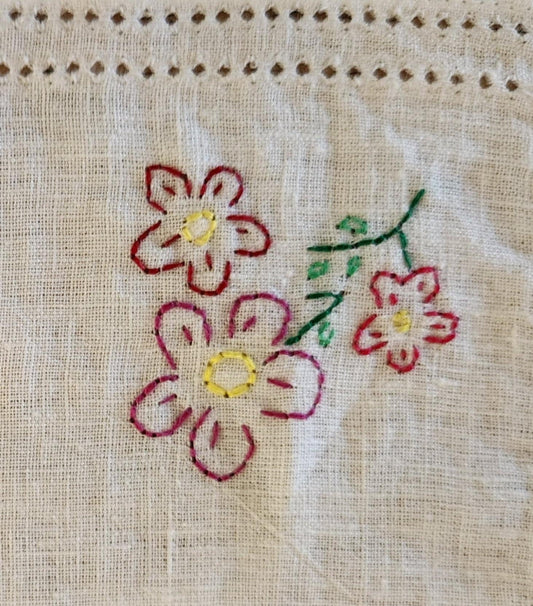 Close up of a white cotton table topper corner with pink, purple and yellow flowers and green leaf's