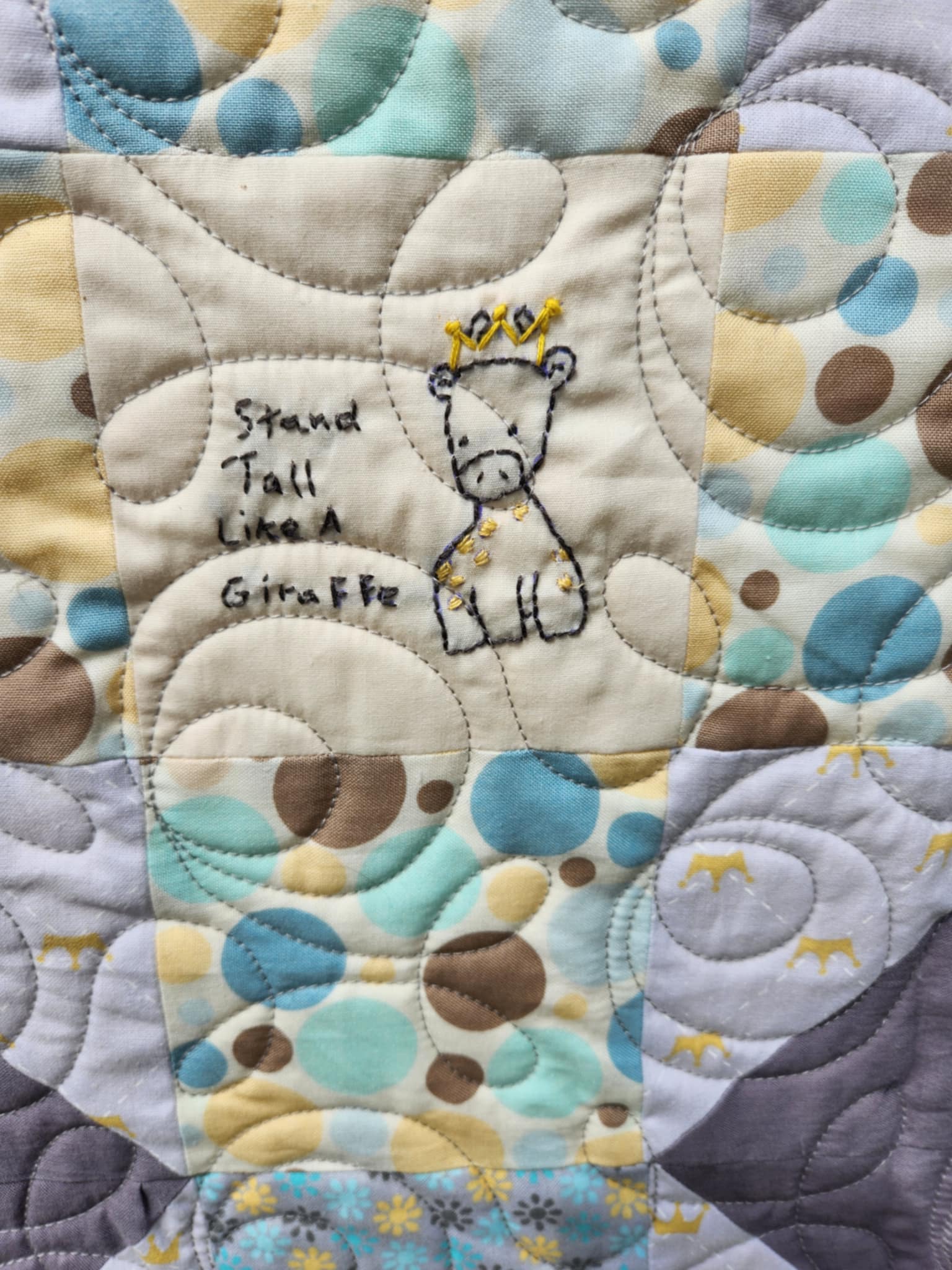 A close up on the hand embordered giraffe With a gold crown and the words stand tall like a giraffe