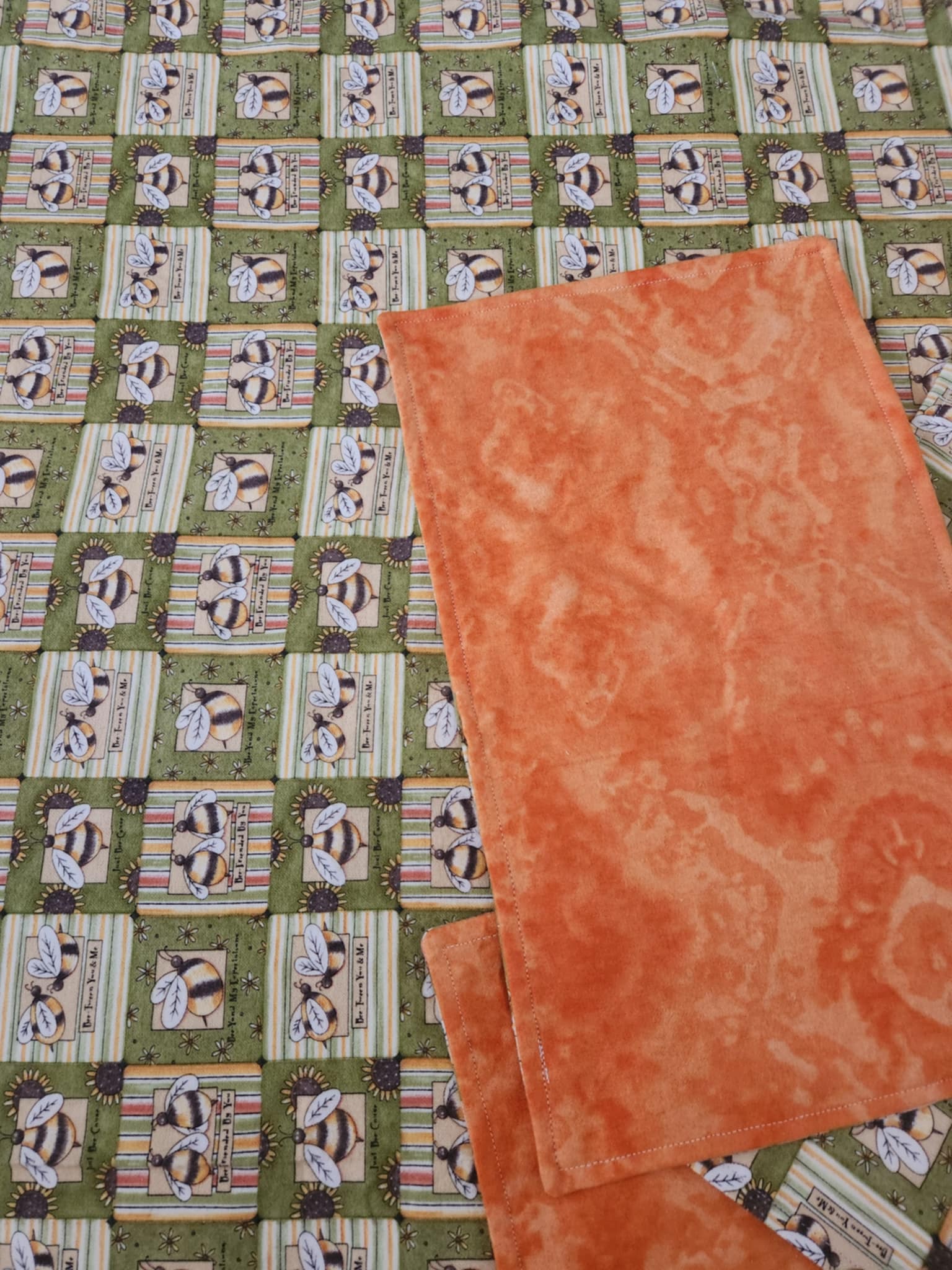 Close up on Green receiving blanket with two green burp rags. With a bee pattern and orange marbling back