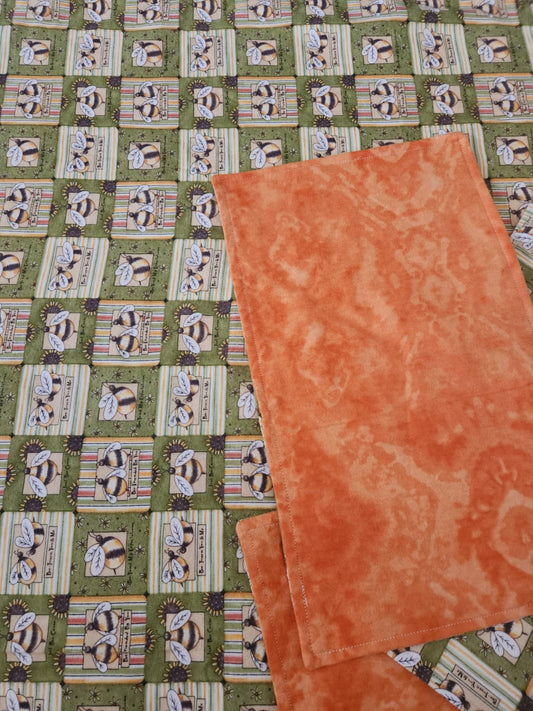 Close up on Green receiving blanket with two green burp rags. With a bee pattern and orange marbling back