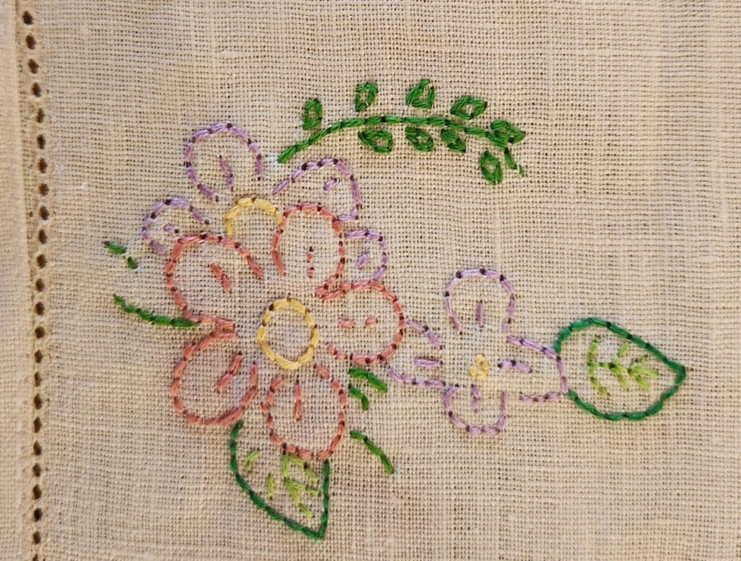 Close up of a white cotton table topper corner with pink, purple and yellow flowers and green leaf's