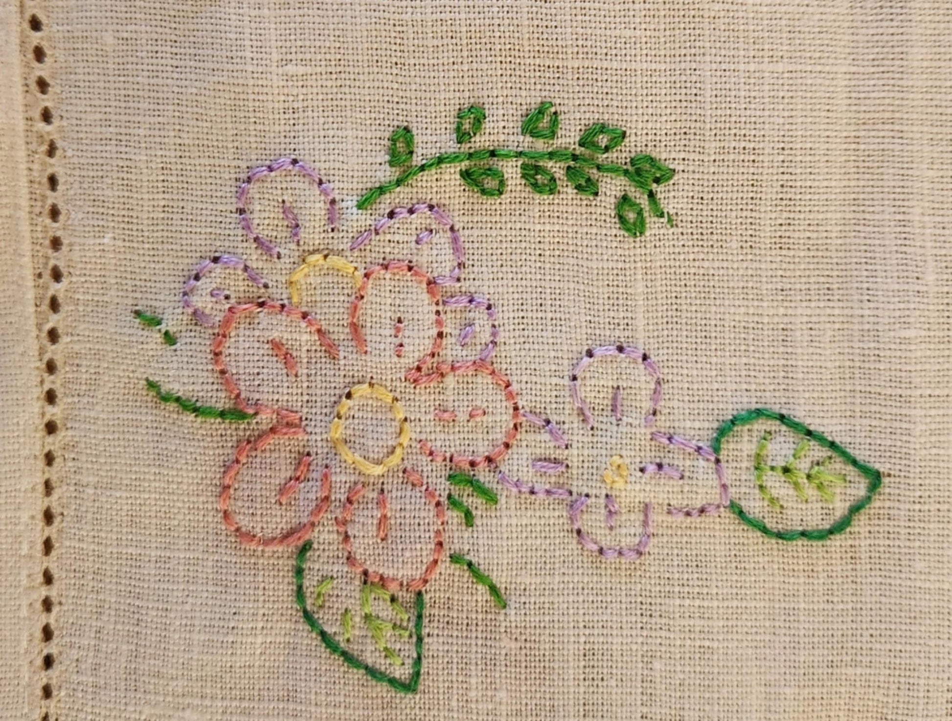 Close up of a white cotton table topper corner with pink, purple and yellow flowers and green leaf's