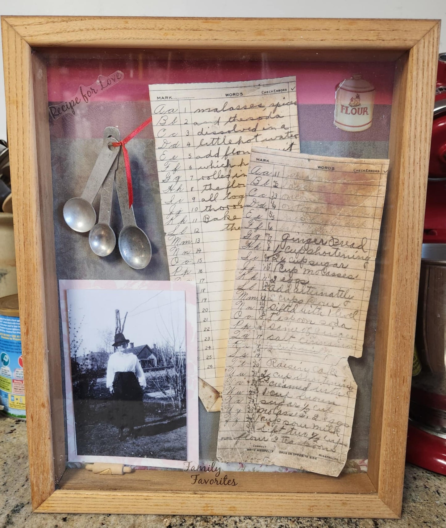 A shadow box with two pages of recipes, an old teaspoon set and a old photo of a woman
