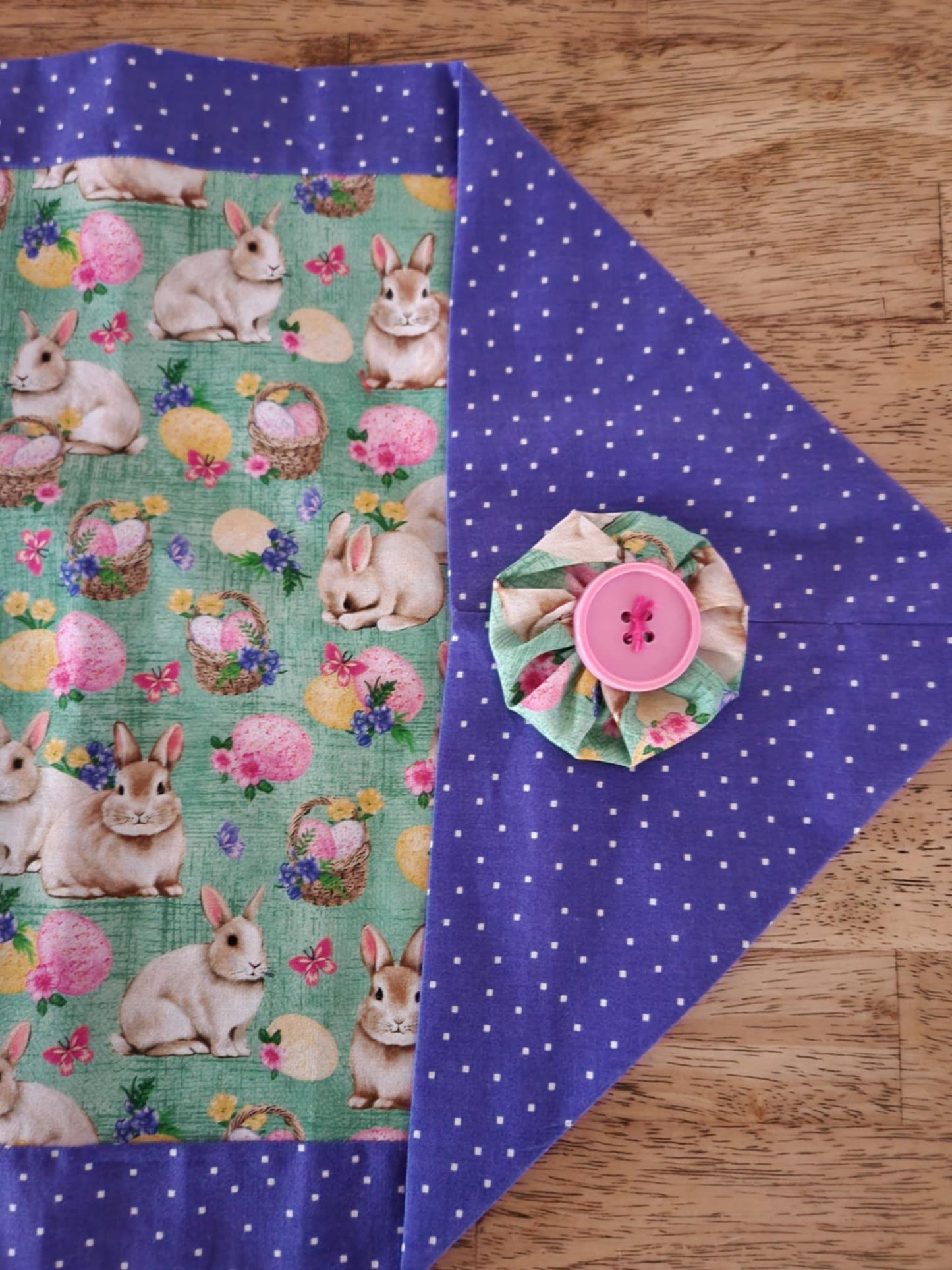 Corner table runner with bunnies' with baskets filled with Easter eggs  in the middle surrounded with a purple poke-a-dots outside with a pink button