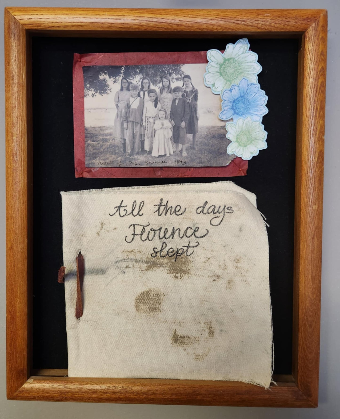 Wood shadow box with a old looking photo with multiple people in it with three flowers along the side. a home made book that looks rough and says All the days Florence Slept