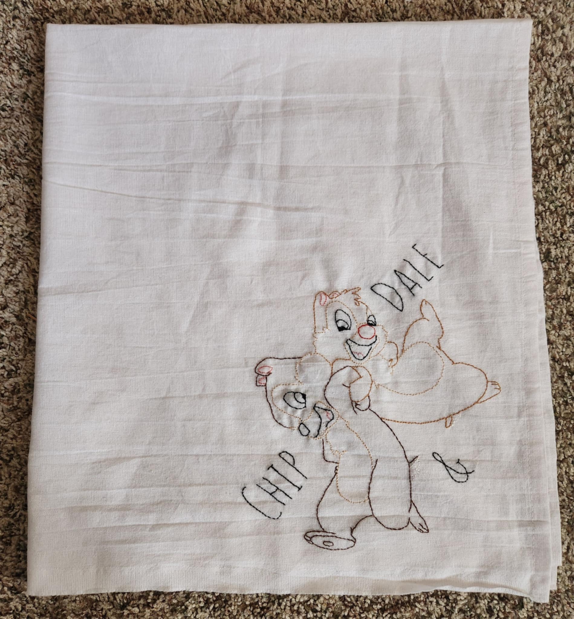 Folded White Dish Towel embroidered  Chipmunks Chip and dale arms entwined. The words " Chip And Dale embroidered in black thread on both sides