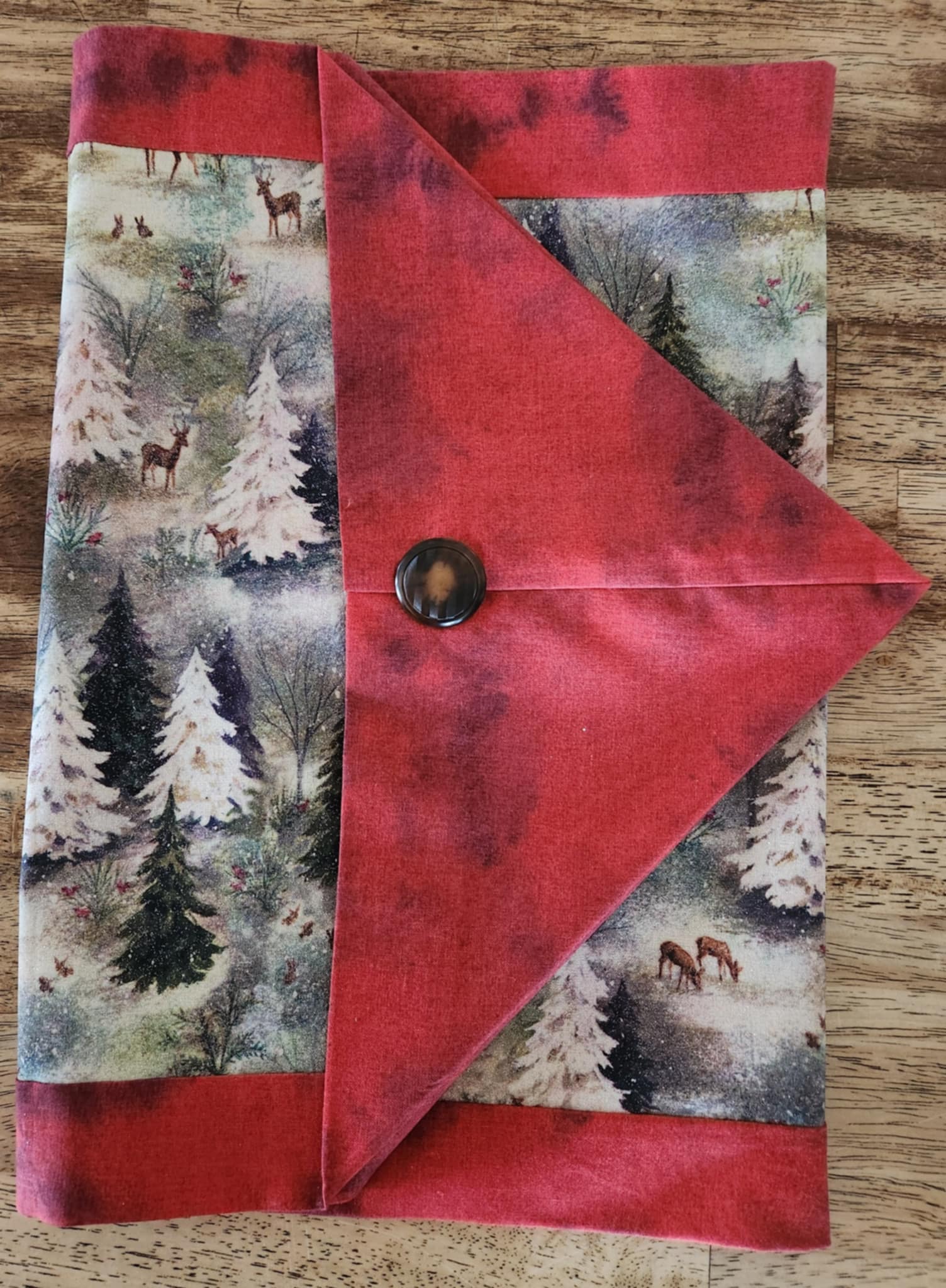 A Folded table runner with deer's and trees in the middle surrounded with a red outside.