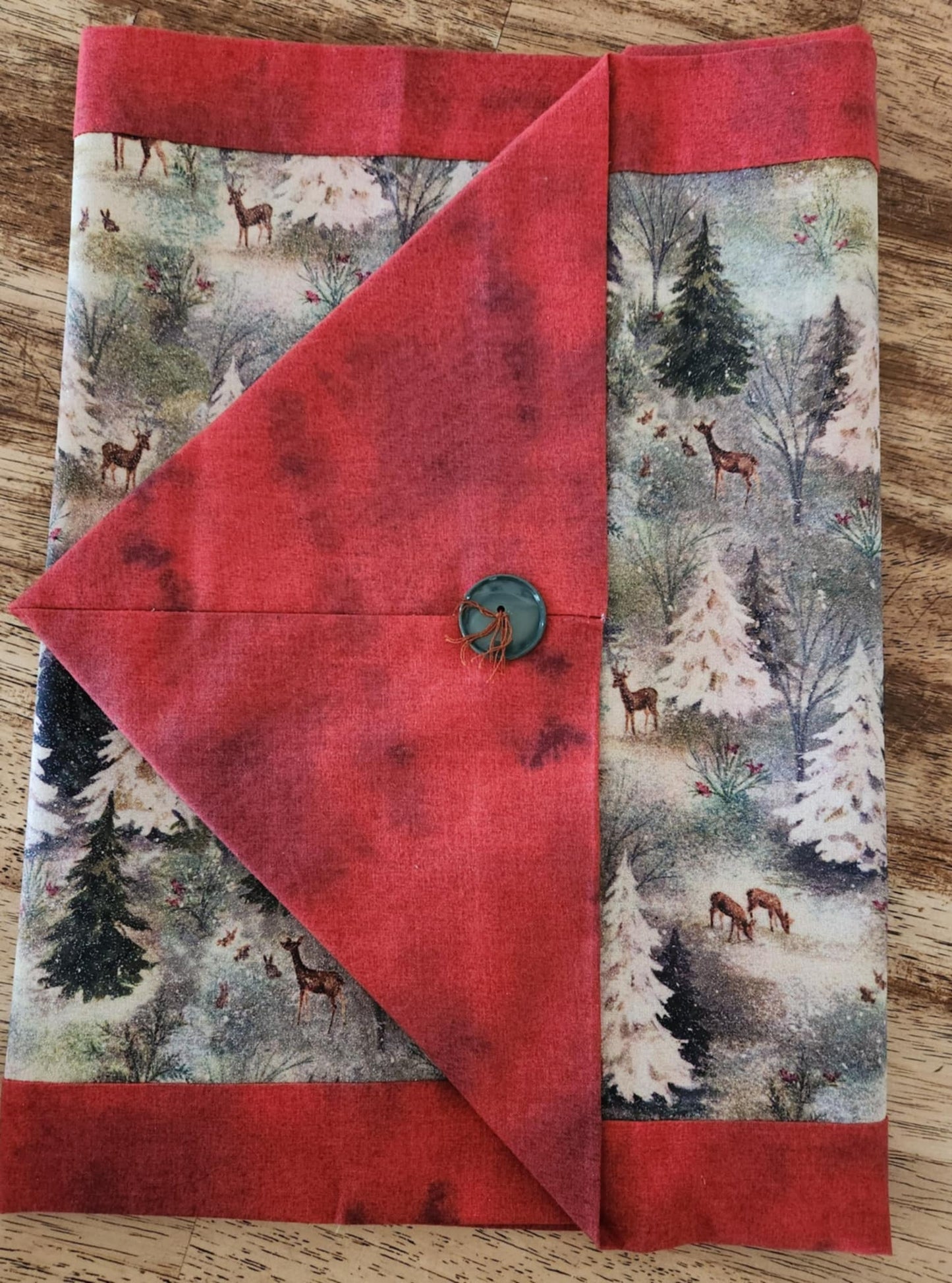 A Folded table runner with deer's and trees in the middle surrounded with a red outside.