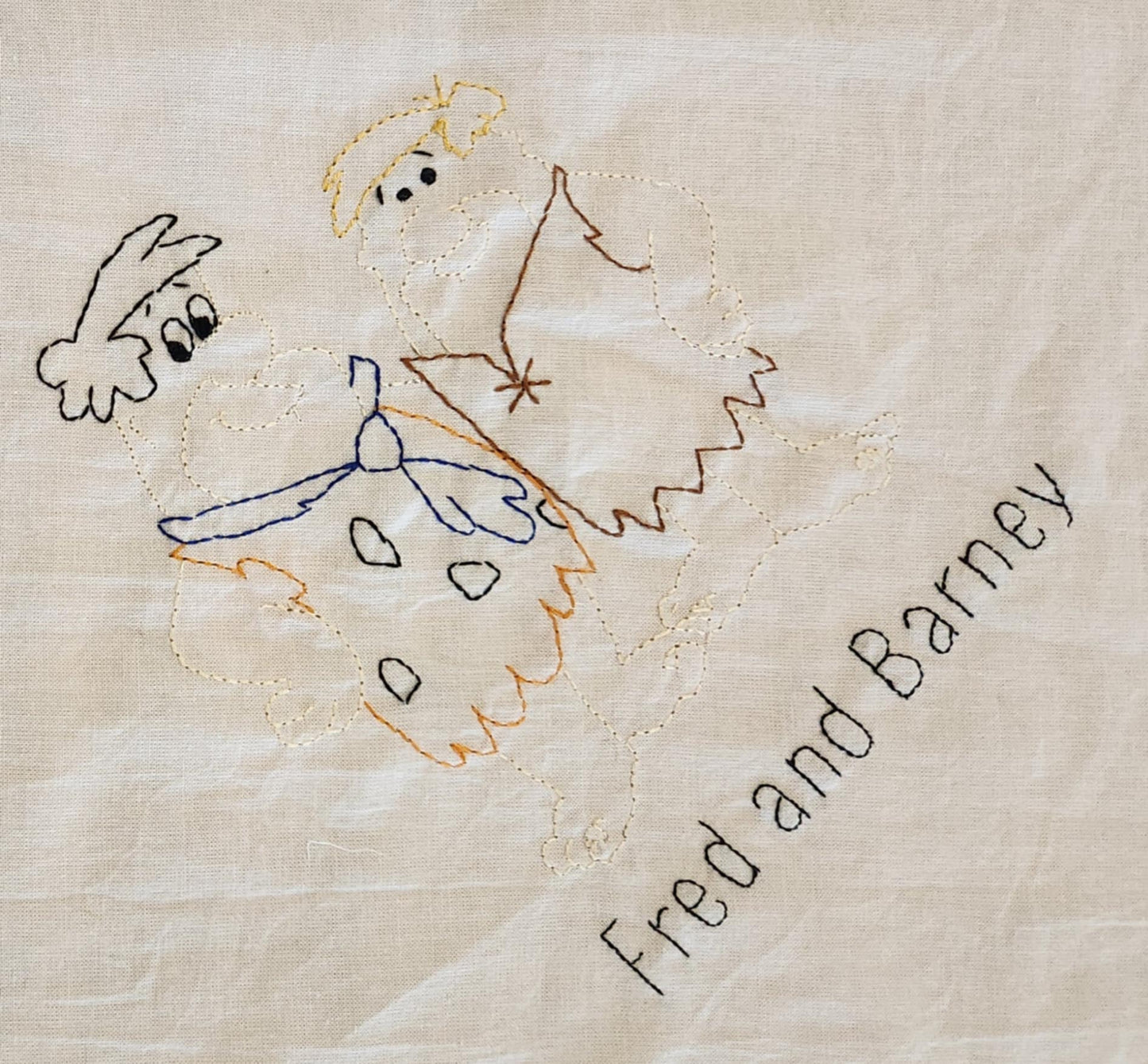 A close up on a white cotton towel With the words Fred and Barney in black thread. Above that is the image of the characters with colored thread.