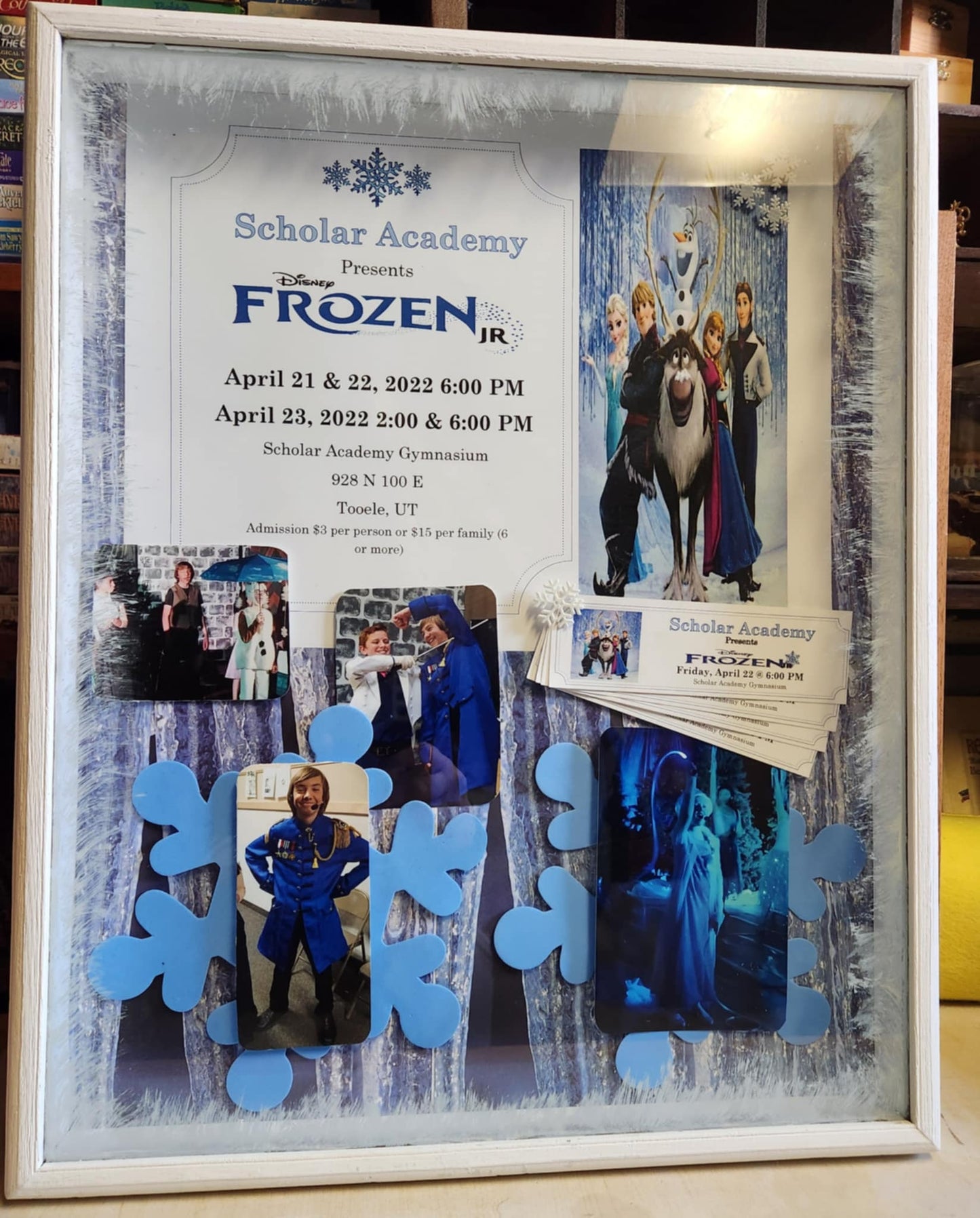White wood Shadow Box with the frozen program, four photos of the cast, picture of the cartoon frozen cast and tickets from the show