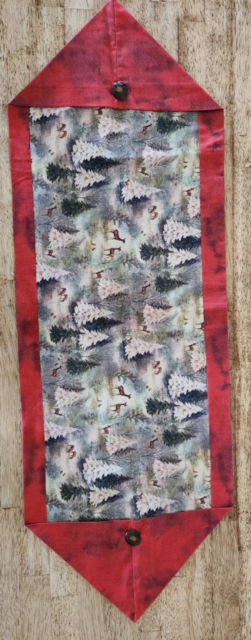 A table runner with triangle ends and the border is red. The inside is trees and deer with sparkle patterns