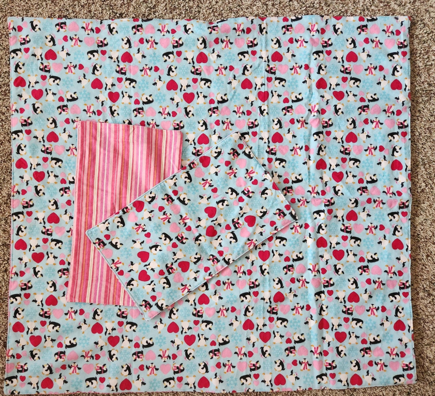 Square Receiving Blanket with Penguins, red and pink hearts with a blue background Fleece. With two burp rags made from the same fabric with the backside with Red, pink and white Strips fabric on top of the blanket