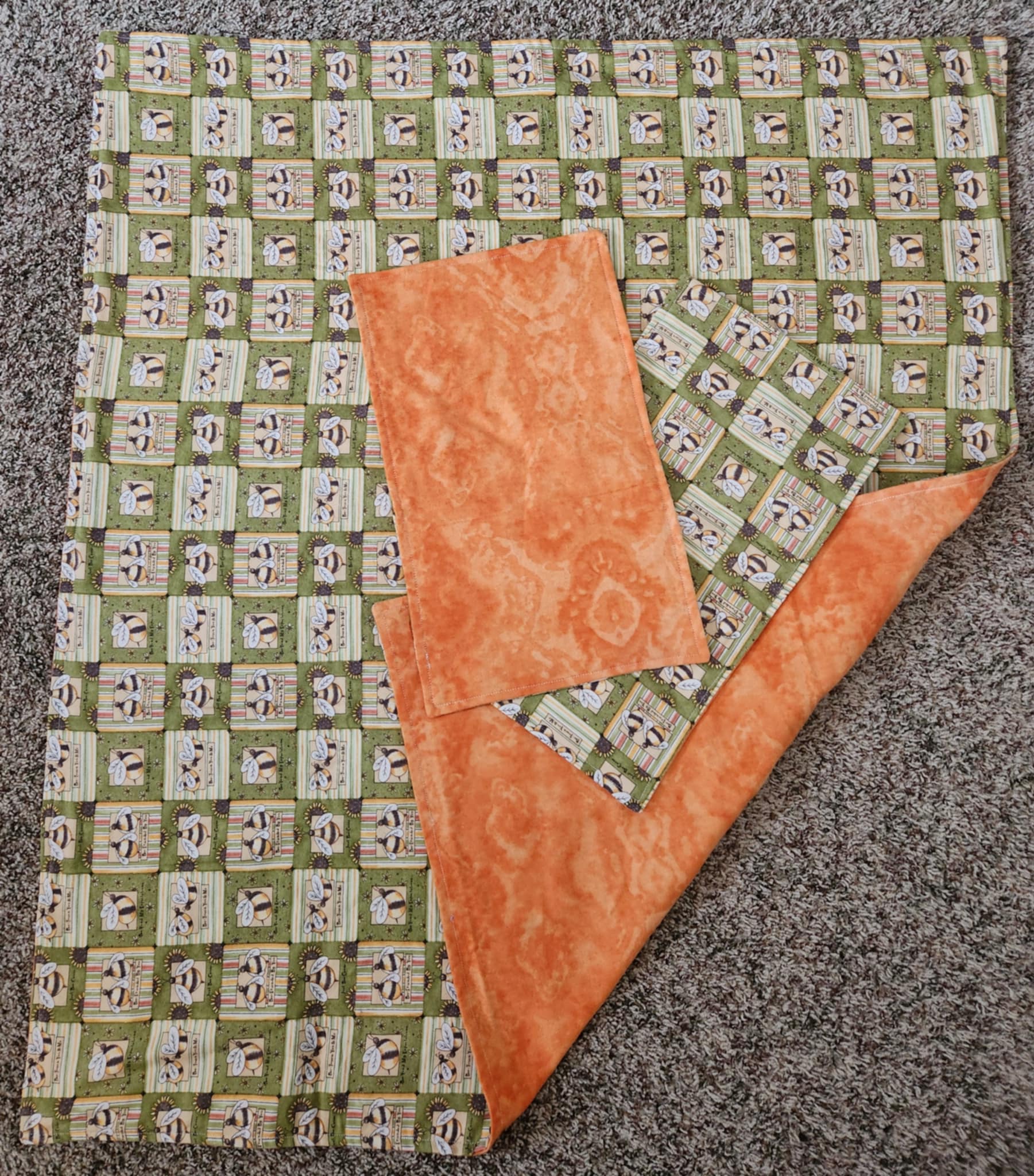 Green receiving blanket with two green burp rags. With a bee pattern and orange marbling back