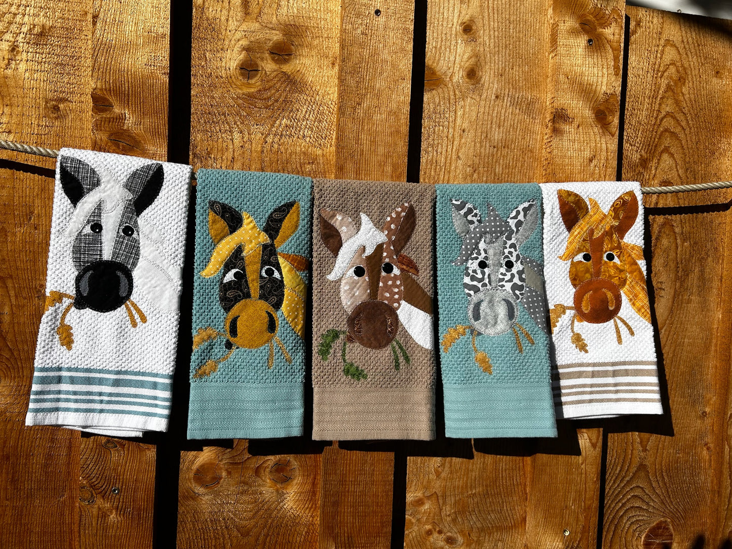 Five Towels With Horses on them. Two blue, two white and one Tan Towel. Each horse is a different color with two grain plants in in there mouth