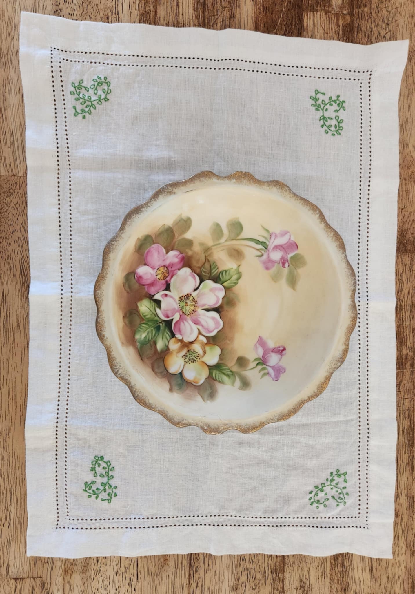 White cotton rectangle table topper with a border of small dots and green embordered leaf's in each corner.