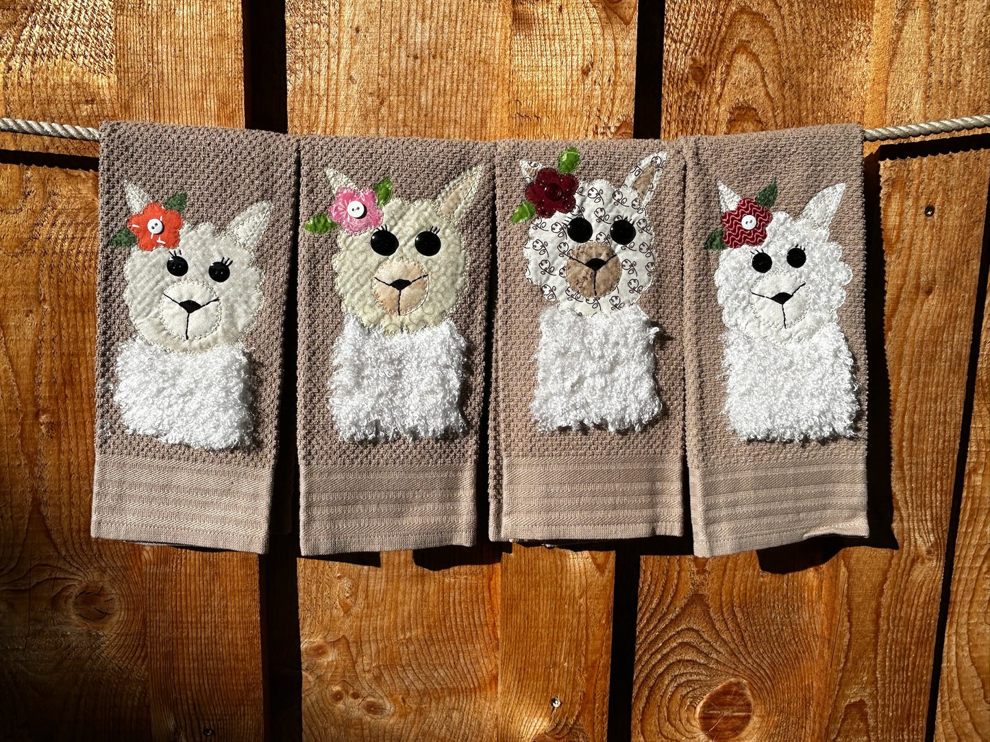 Four dish towels all brown. Each llama is white and fluffy but have a different color and pattern flower on there Left ear