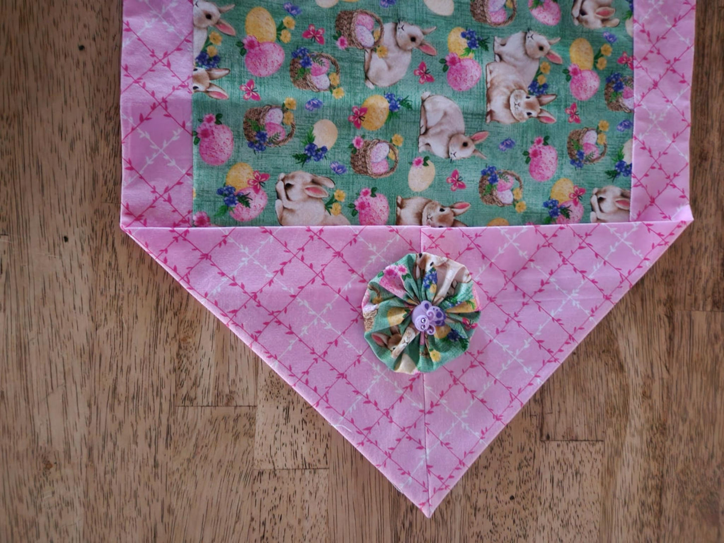 A corner table runner with bunnies' with baskets filled with Easter eggs  in the middle surrounded with a pink and white vine fabric outside with a bug button