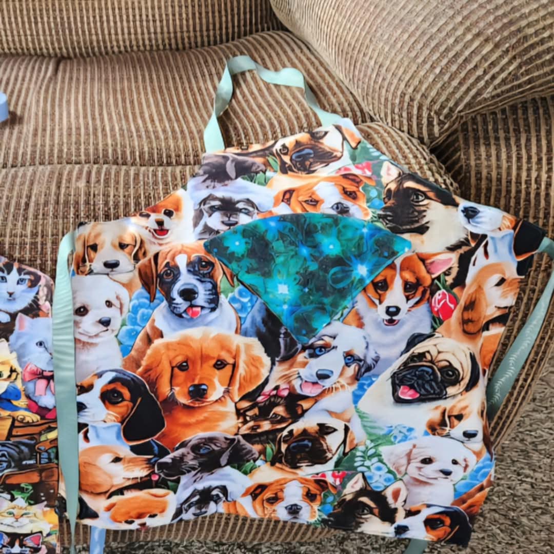 Multicolored child apron with images of puppies and a blue and black pocket in the center.