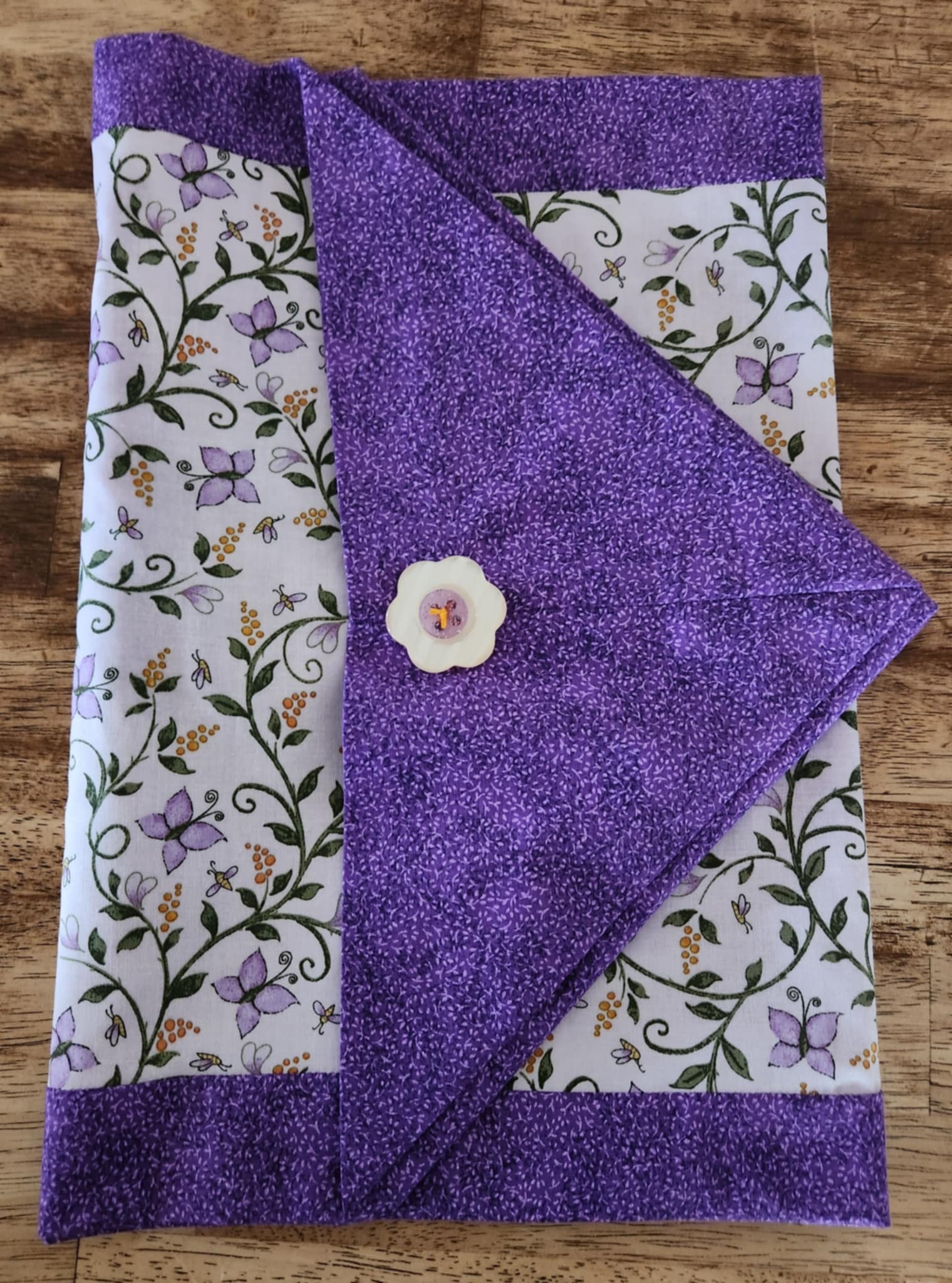 A Folded table runner with butterfly's and flowers in the middle surrounded with a purple outside.