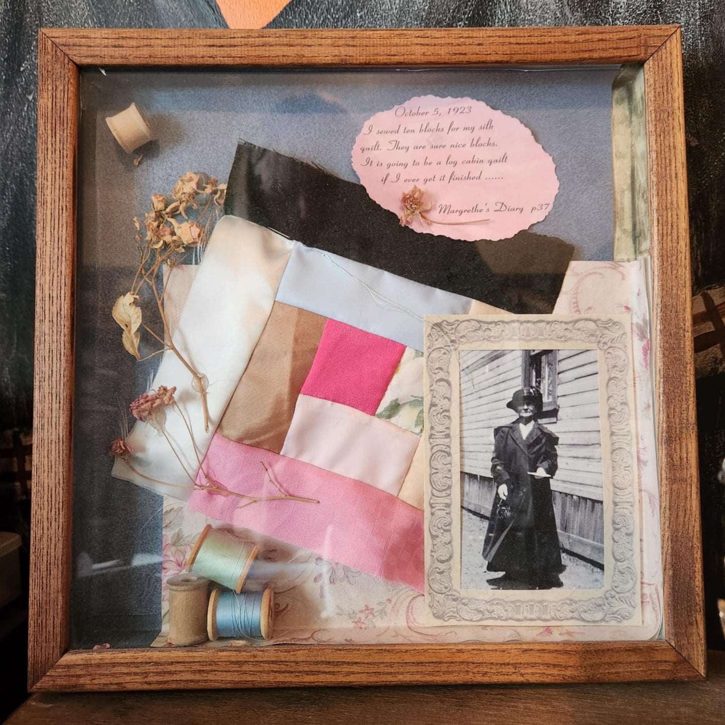 A wood shadow box with a square quilt block, With three things of thread and a old photo of a woman