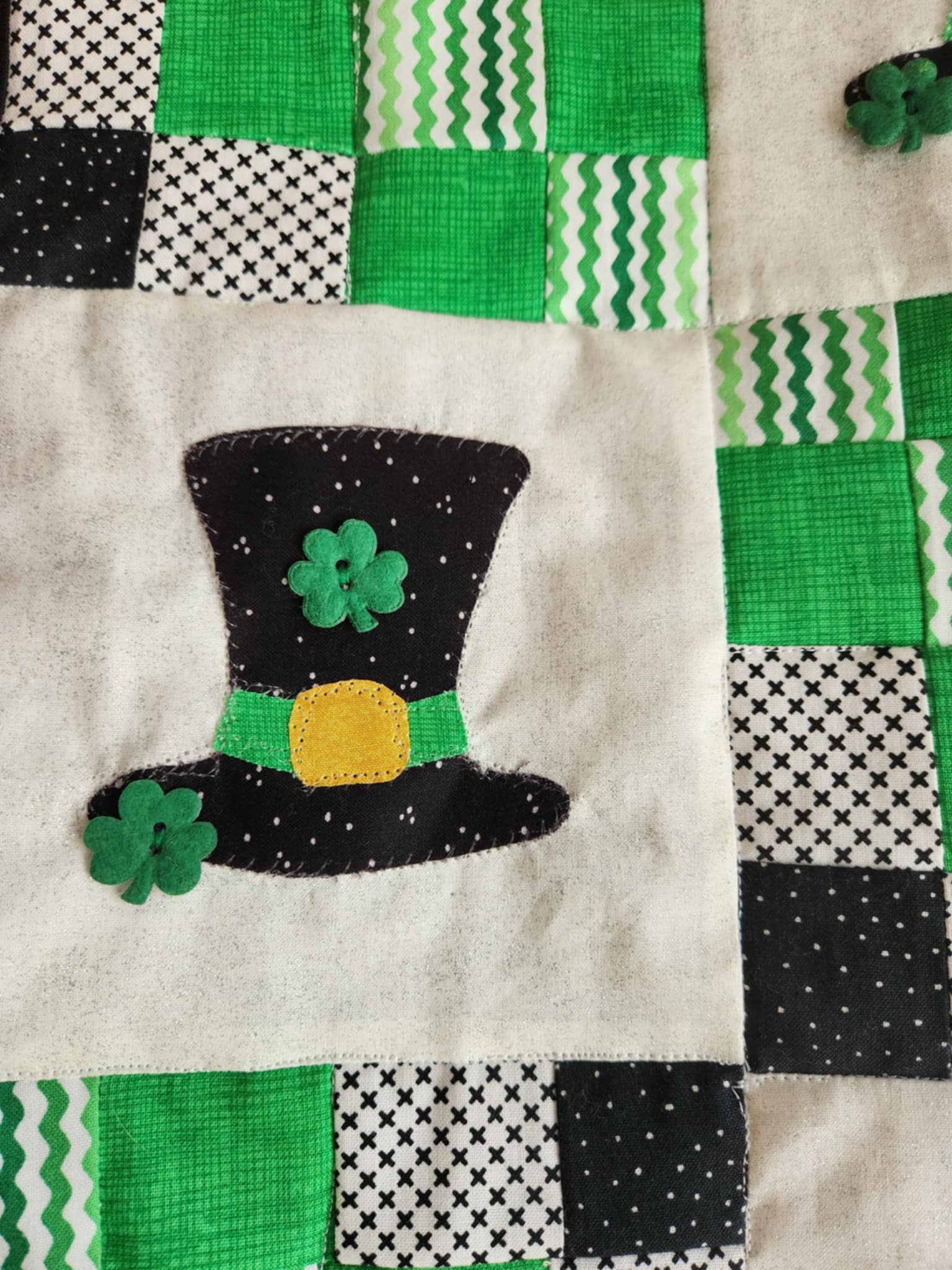 Black leprechaun hat with shamrock buttons on a white background with green, black and white squares