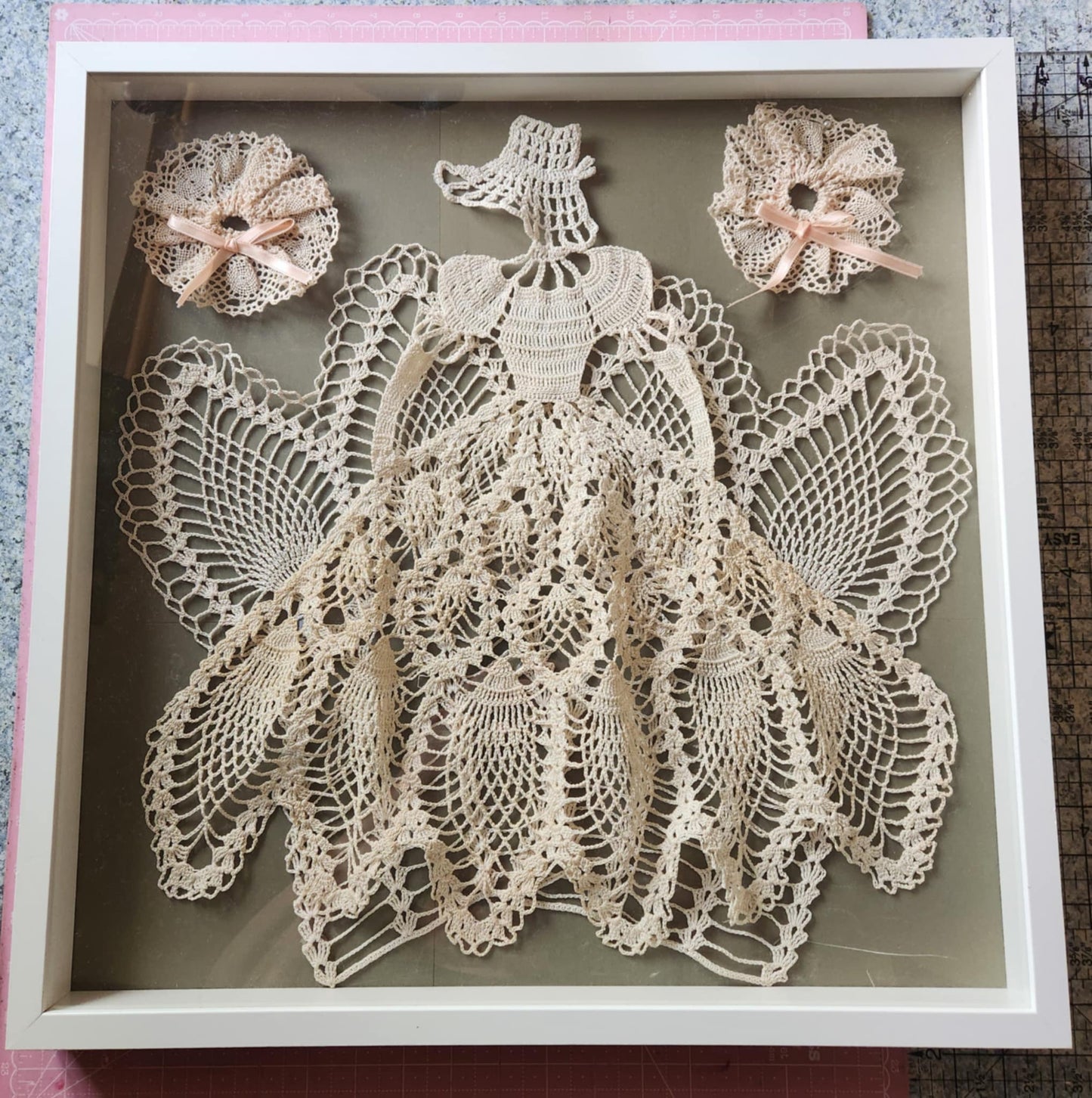 A shadow box with white tatting thread made in to a ball gown and bonnet