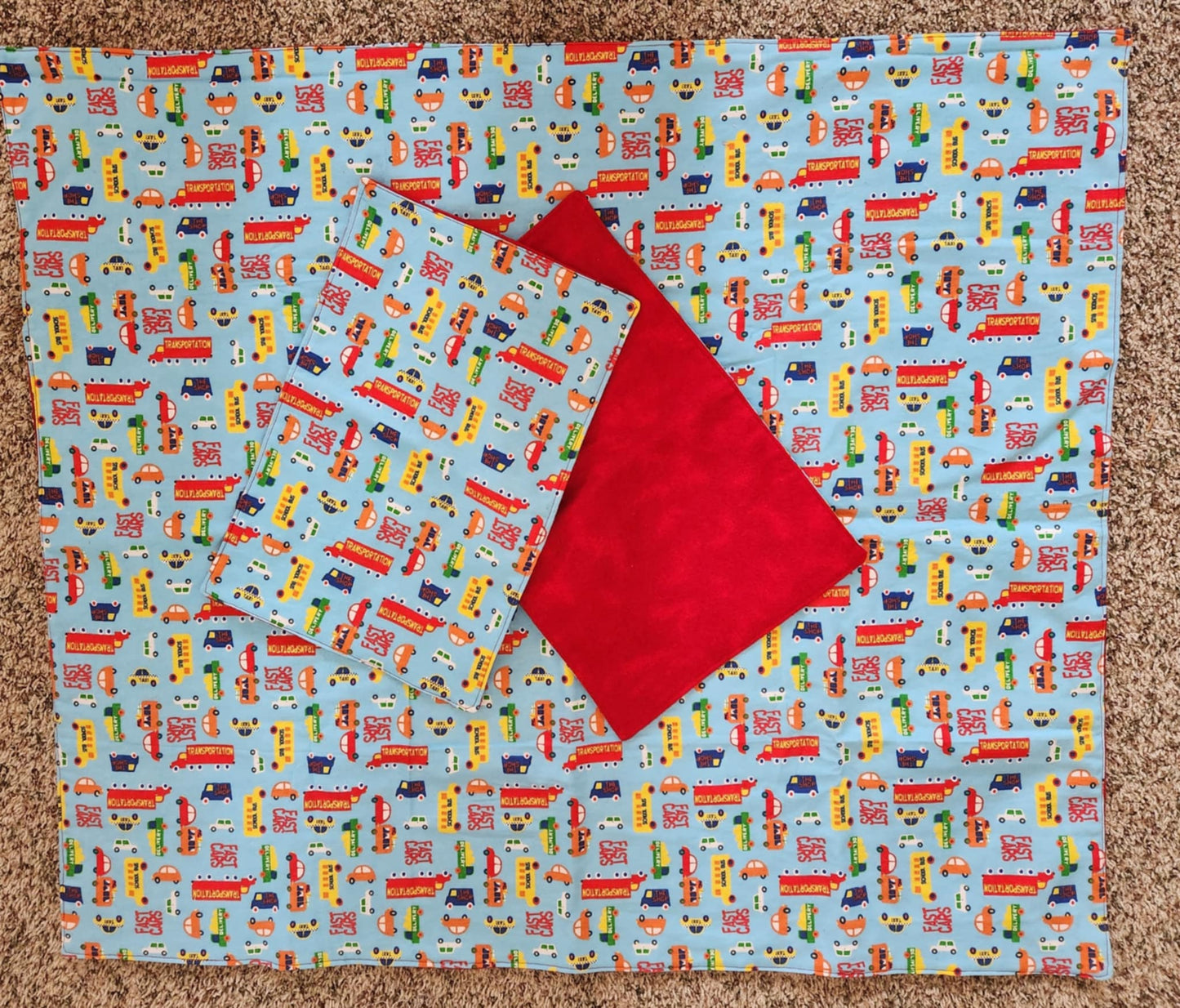 Square Receiving Blanket with Multi Vehicles with a blue background Fleece. With two burp rags made from the same fabric also showing red back on top of the blanket