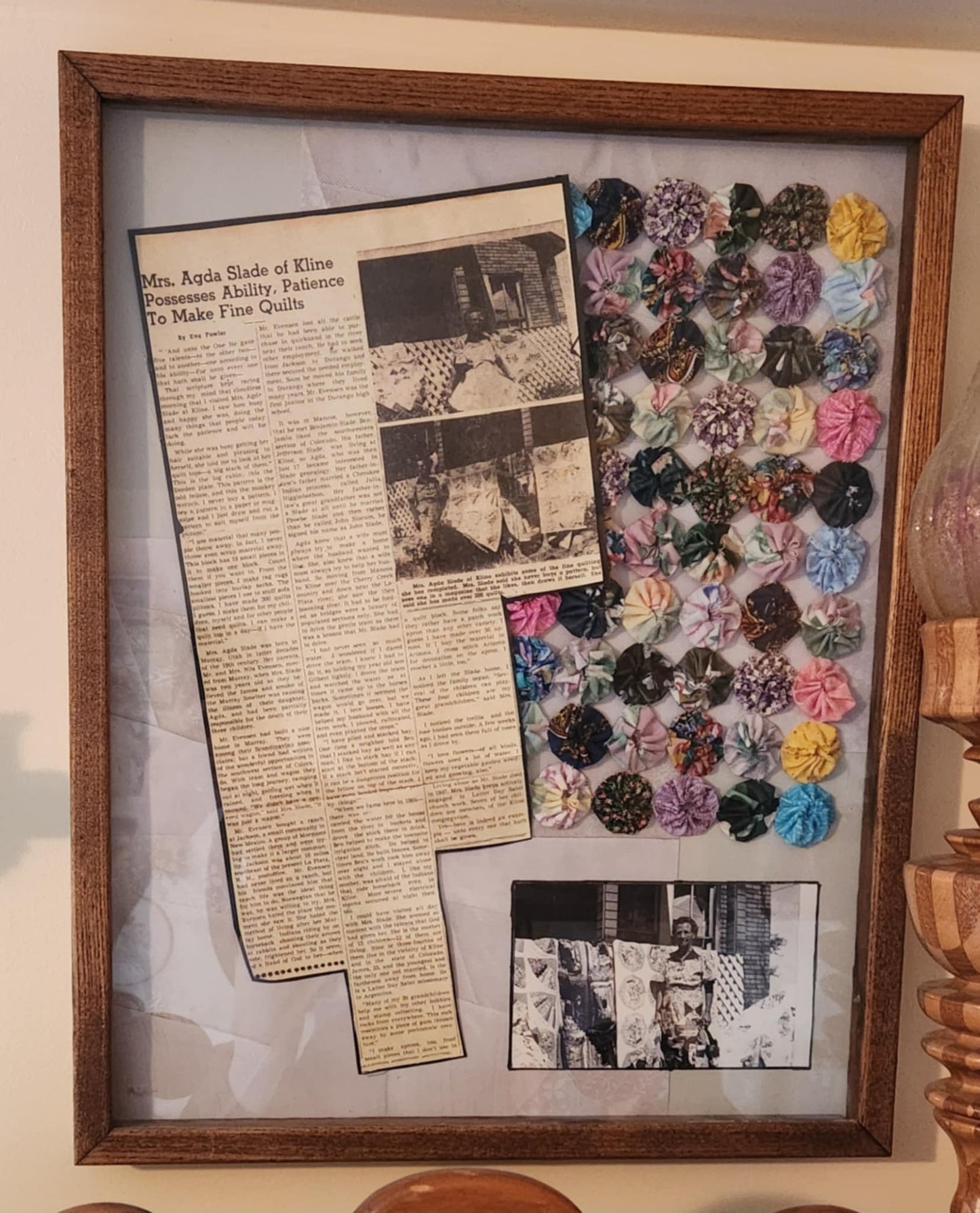 A wood shadow box with a newspaper cut out, part of a yoyo quilt and old photo of a woman and a quilt
