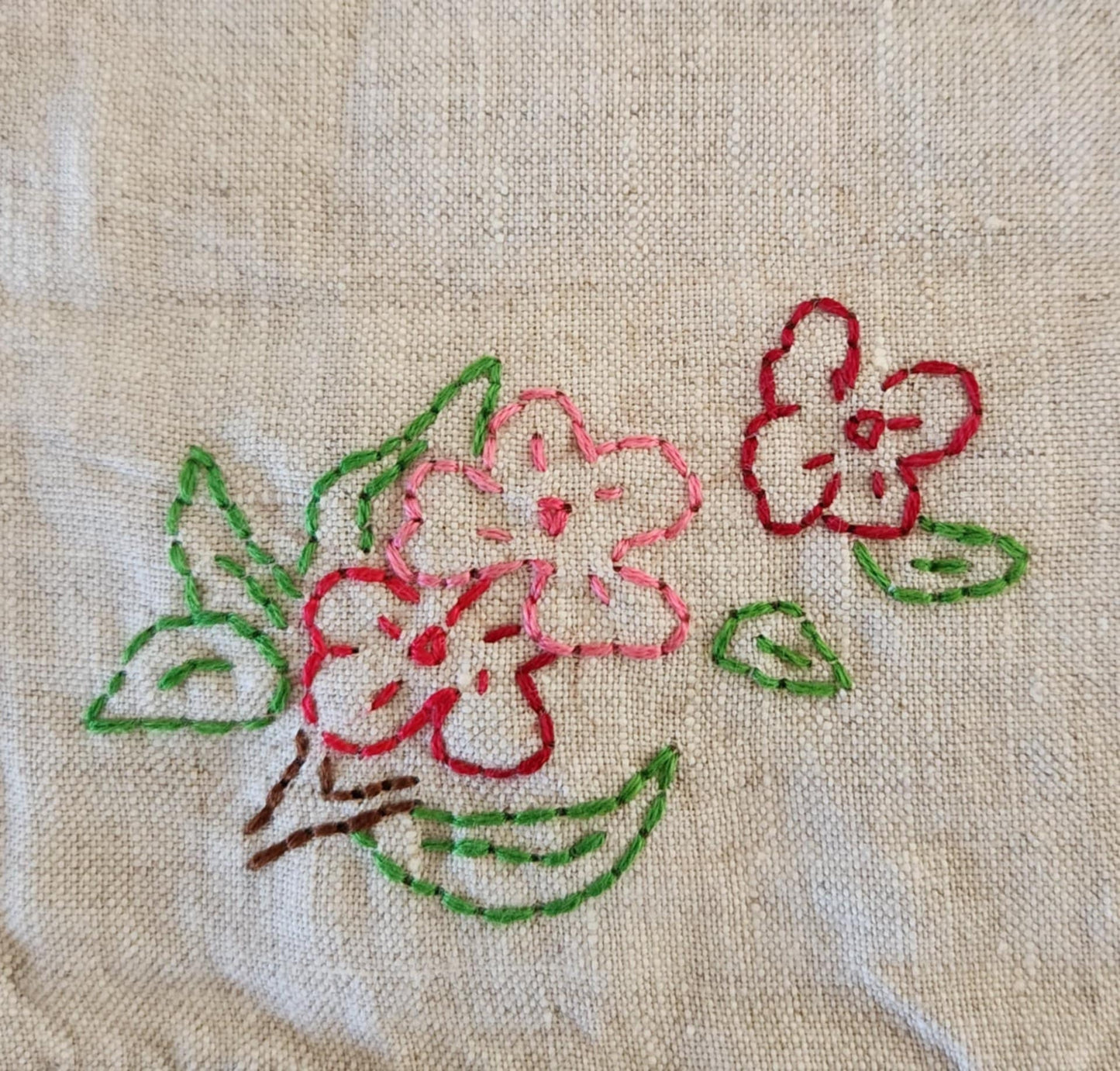 Close up of a white cotton table topper corner with pink, purple and yellow flowers and green leaf's