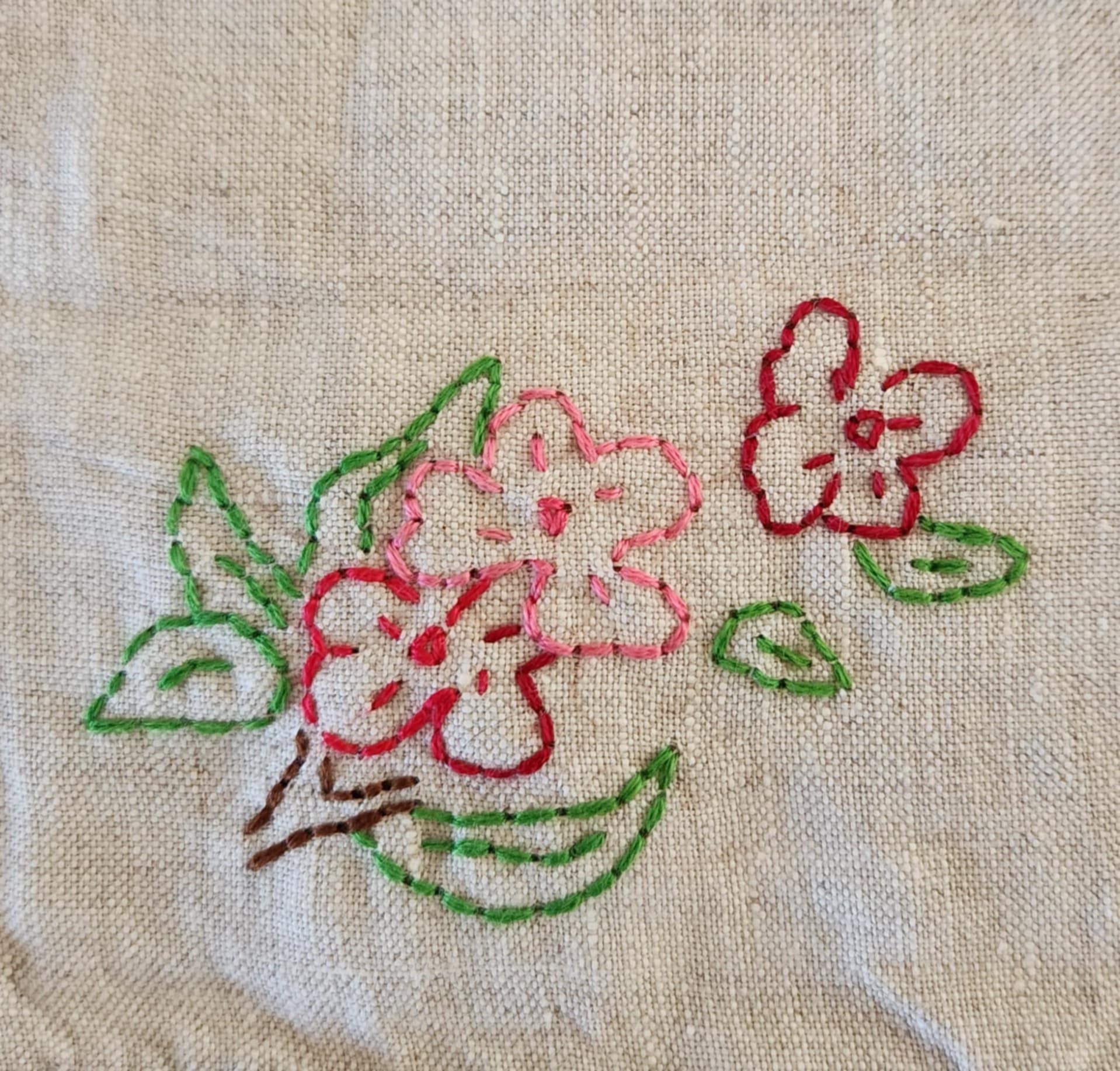Close up of a white cotton table topper corner with pink, purple and yellow flowers and green leaf's
