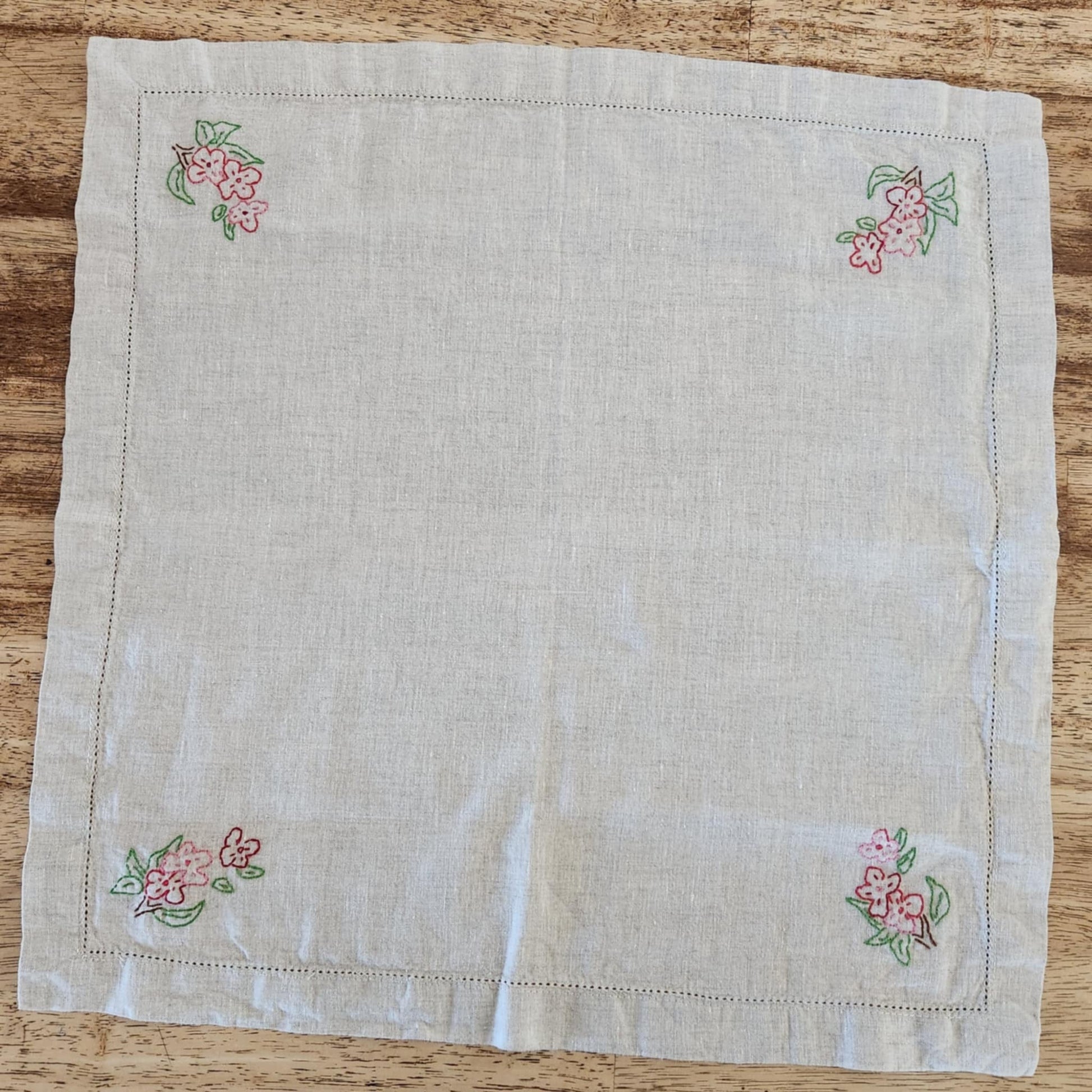 White cotton square table topper with a border of small dots and pink, purple and yellow flowers and green leaf's in each corner