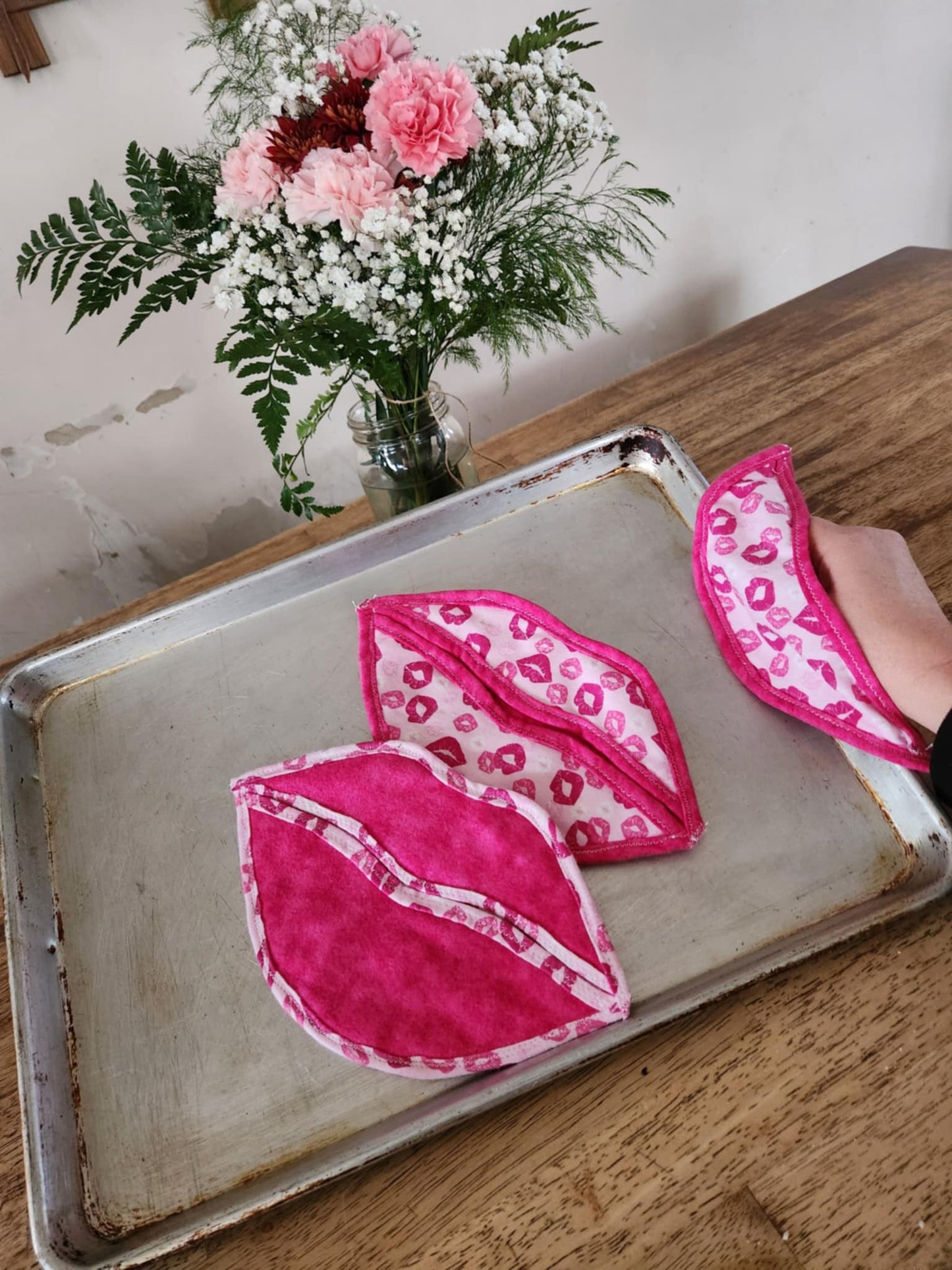 Hot pad shaped like a lips with light pink background with pink kisses seal flap and the rest a bright pink