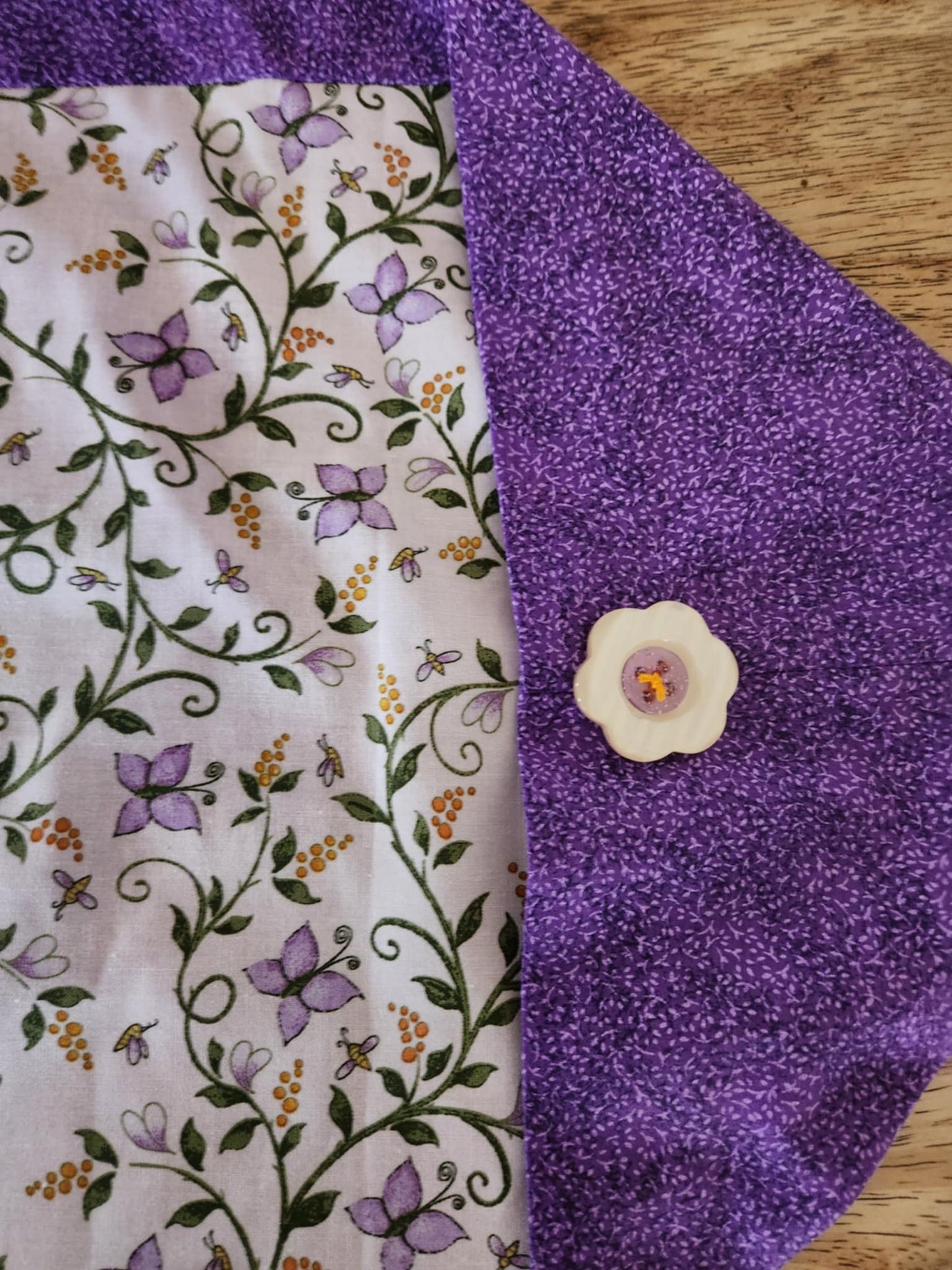 Corner table runner with butterfly's and flowers in the middle surrounded with a purple outside with a flower button