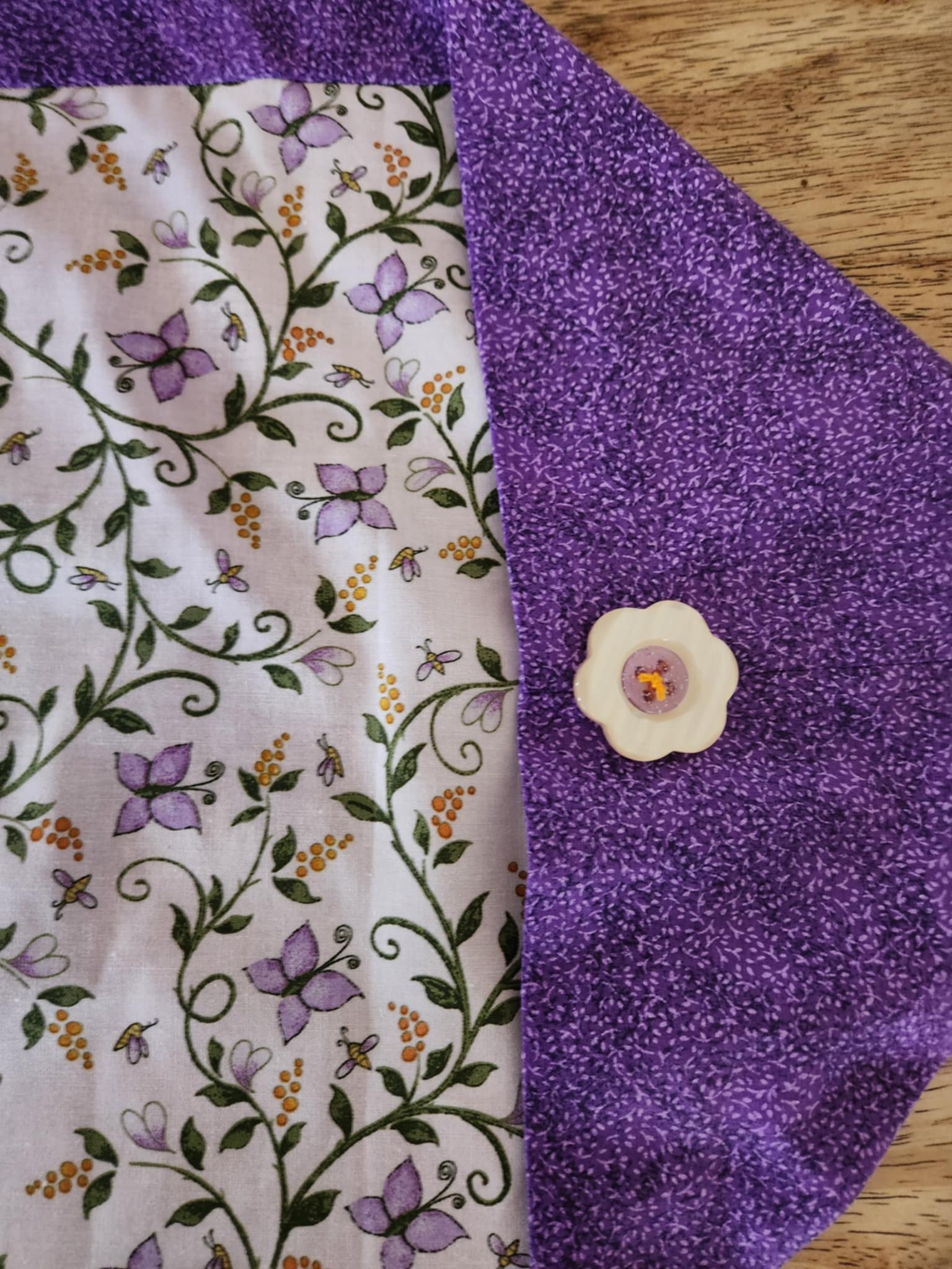 Corner table runner with butterfly's and flowers in the middle surrounded with a purple outside with a flower button