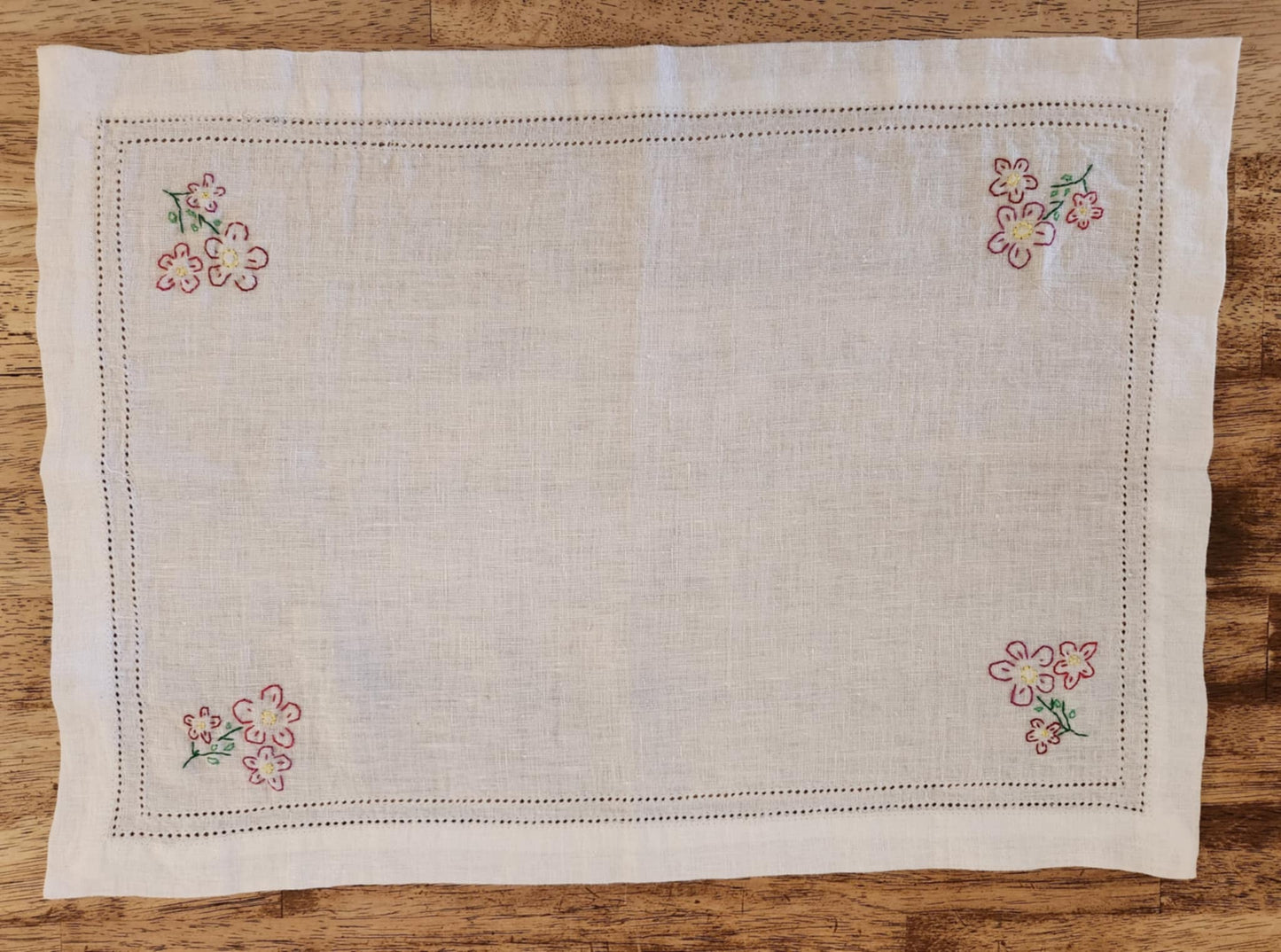 White cotton rectangle table topper with a border of small dots and pink, purple and yellow flowers and green leaf's in each corner