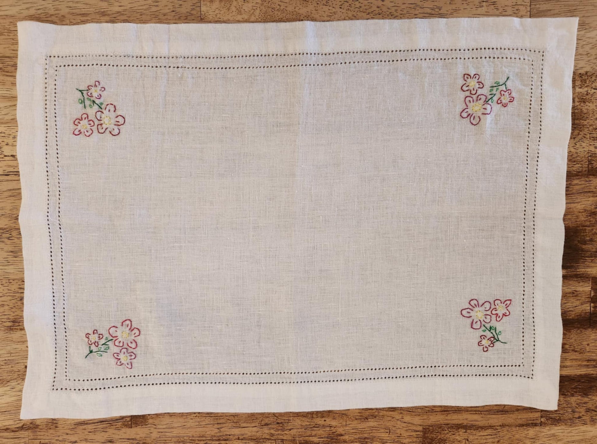 White cotton rectangle table topper with a border of small dots and pink, purple and yellow flowers and green leaf's in each corner
