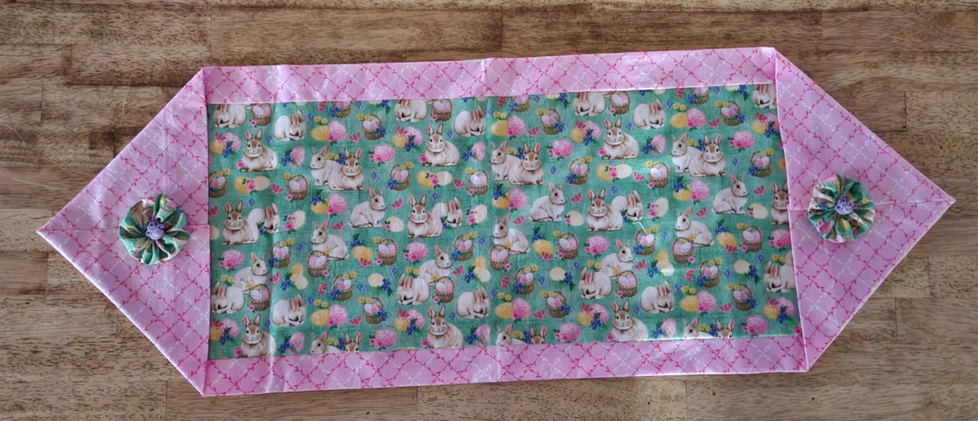 A top view table runner with bunnies' with baskets filled with Easter eggs  in the middle surrounded with a pink and white vine fabric outside with a bug button