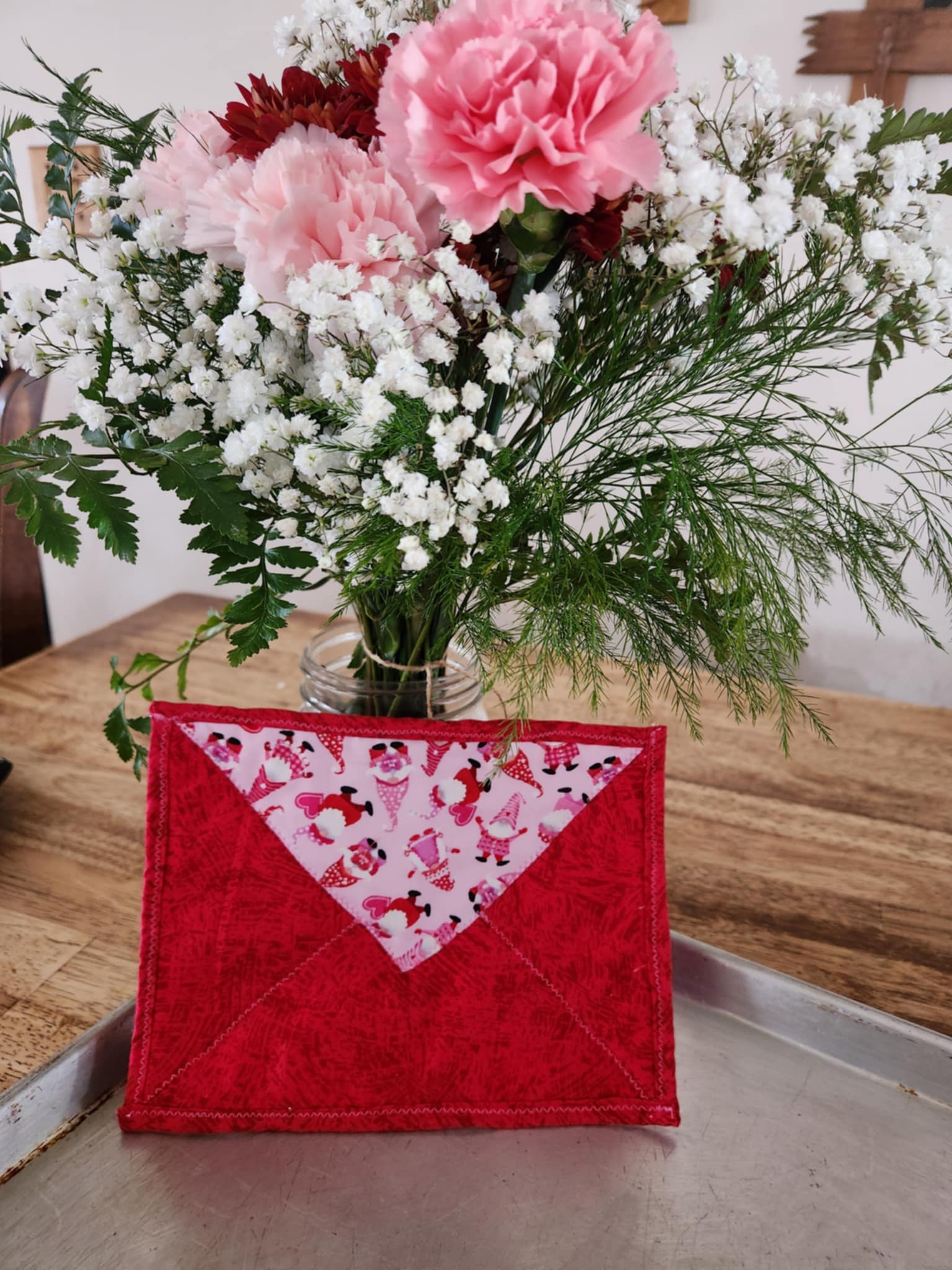 Hot pad shaped like a envelope with light pink background with red and pink gnomes pattern seal flap and the rest is bright red