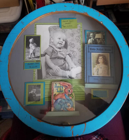A round blue Wood shadow with a photo of a baby boy surrounded by three other photos and two children books