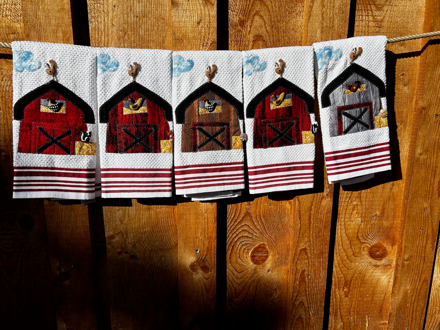 Five white hand towels with a blue and white cloud in the left corner. There are three red barns one brown, and one gray barn