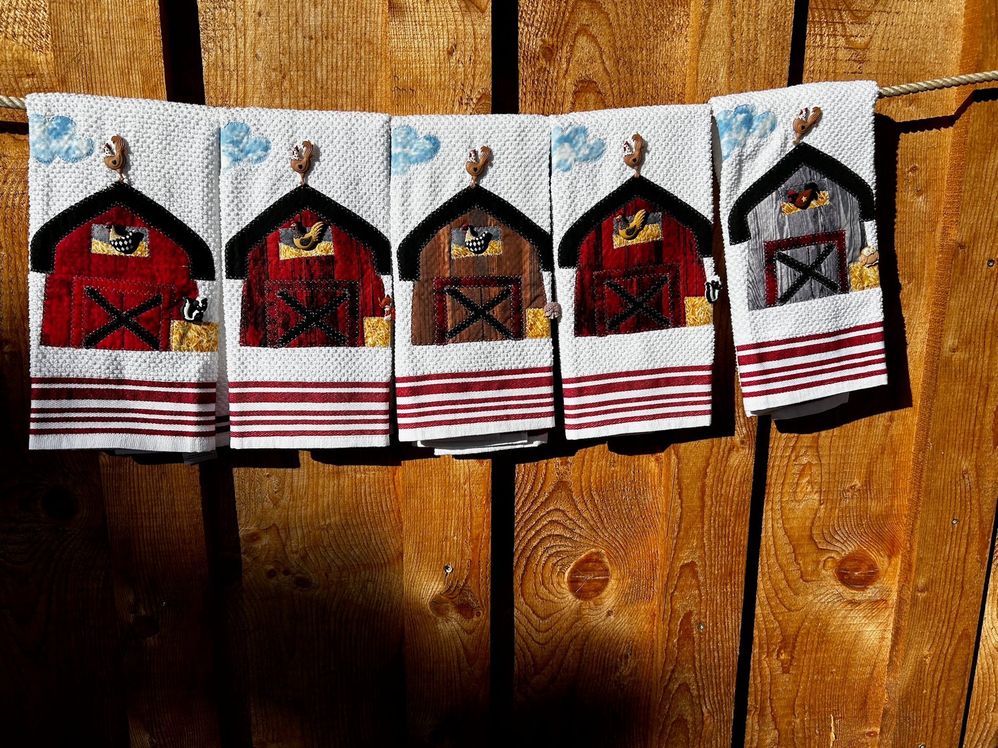 Five white hand towels with a blue and white cloud in the left corner. There are three red barns one brown, and one gray barn