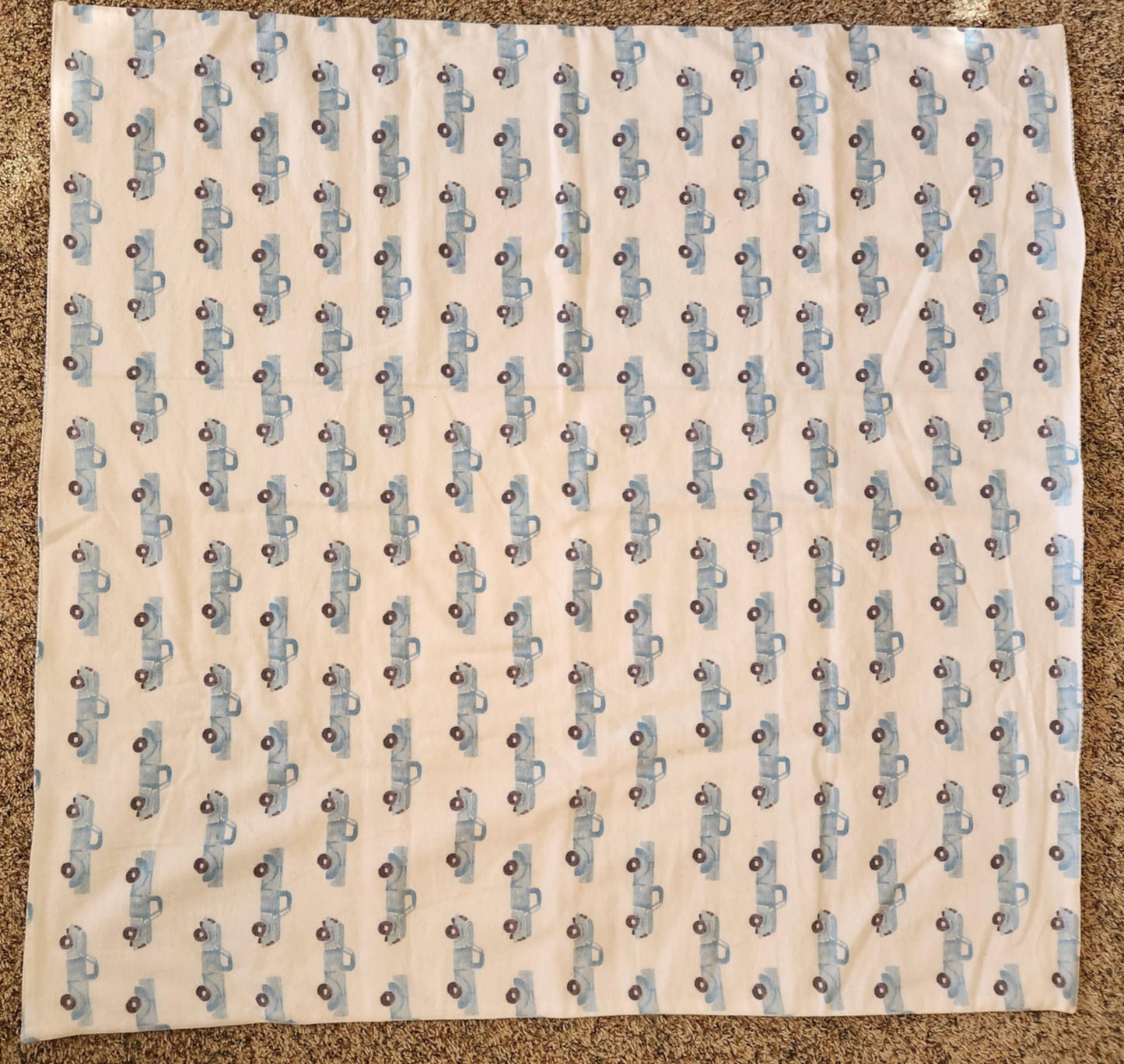 A square flannel receiving blanket with a blue truck pattern, laid out flat.