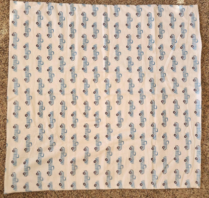 A square flannel receiving blanket with a blue truck pattern, laid out flat.