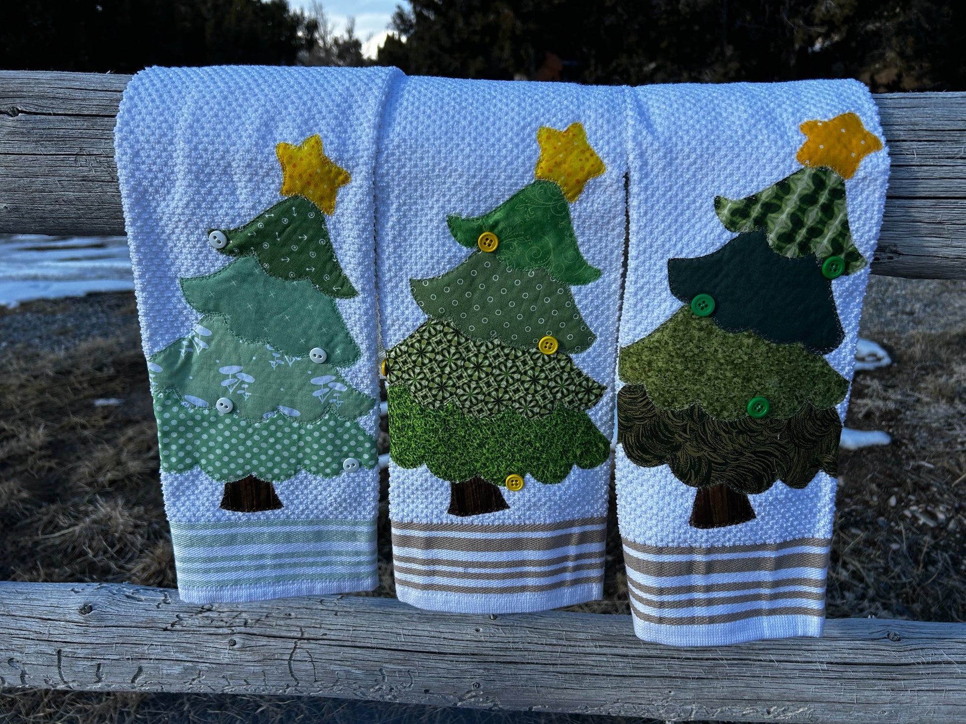 Three white hand towels, each tree is green but different patterns. They have a yellow star on to but are all different patterns