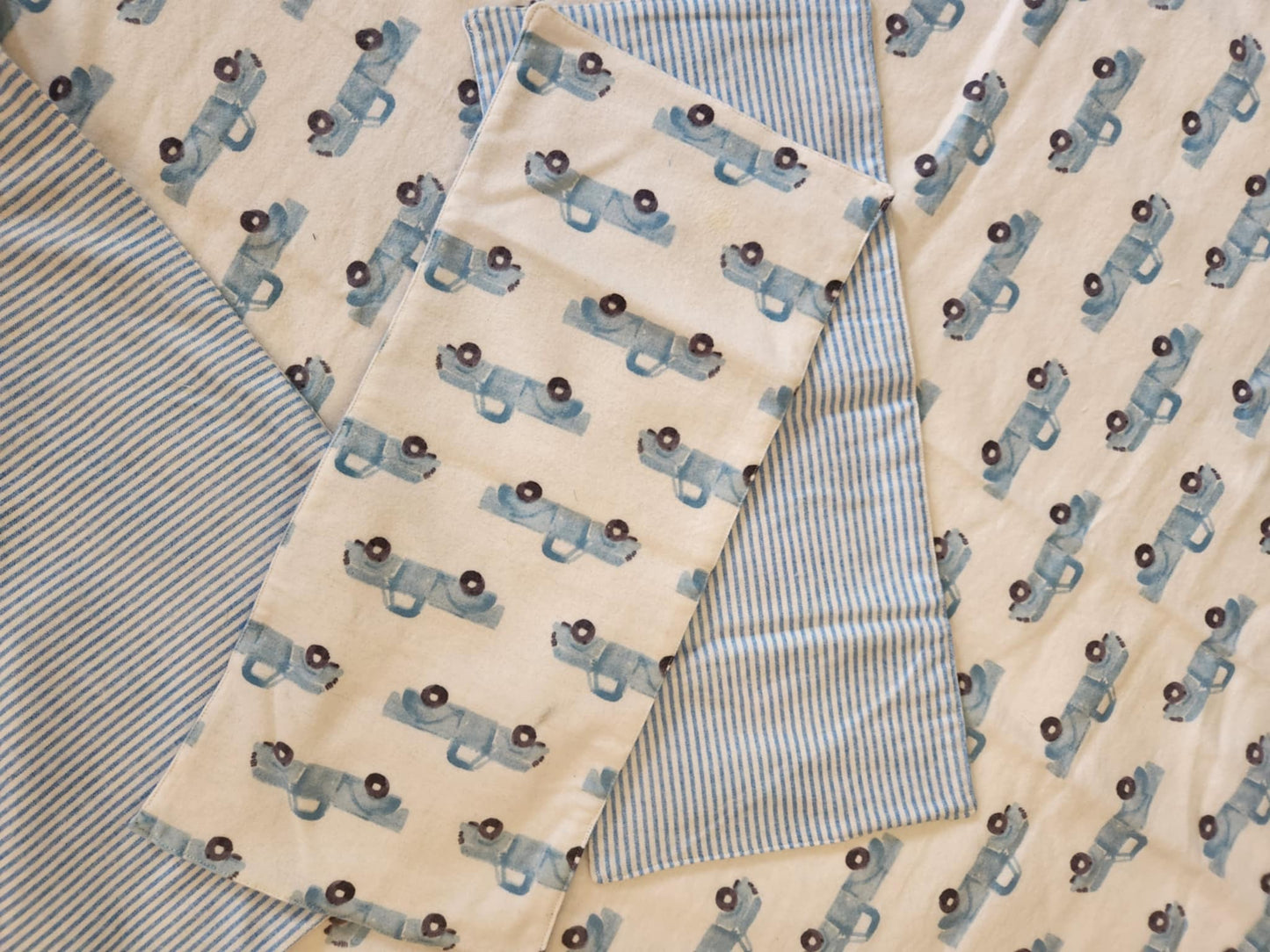 Close up on Receiving Blanket with Baby blue Pick up trucks with white background Fleece. With corner turned down showing baby blue and white Strip fleece. With tow burp rags  made from the same fabric on top of the blanket
