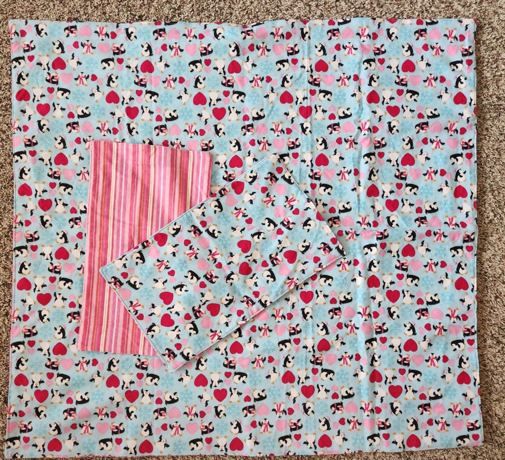 Square Receiving Blanket with Penguins, red and pink hearts with a blue background Fleece. With two burp rags made from the same fabric  with the backside with Red, pink and white Strips fabric on top of the blanket  