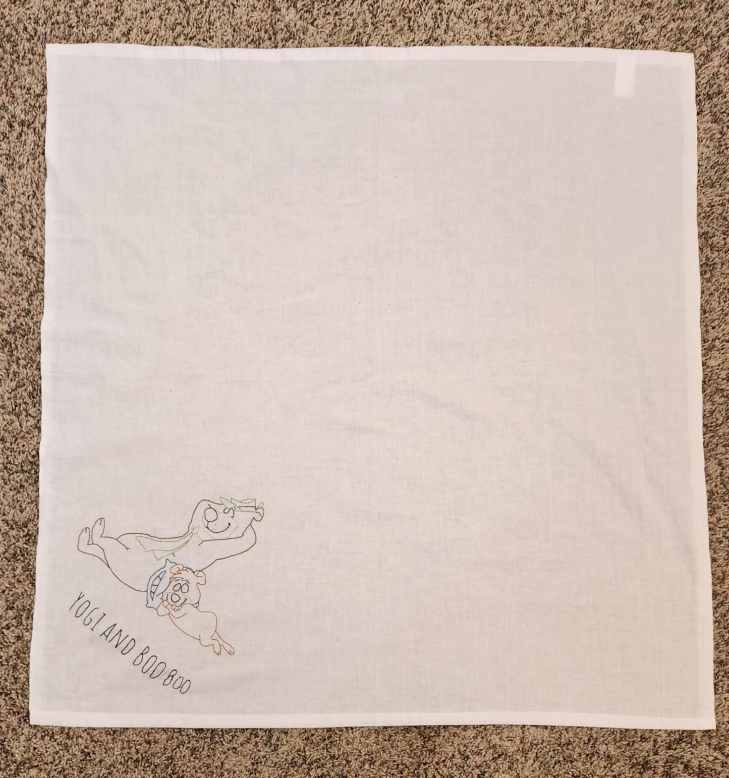 White rectangular towel with Two bears sleeping in the left corner one on a pillow resting on the other. With the words "yogi and booboo" under them