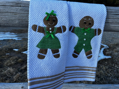 Two White towels one with a gingerbread man in a green outfit. The second one  s a gingerbread woman in a green dress with a green ribbin bow